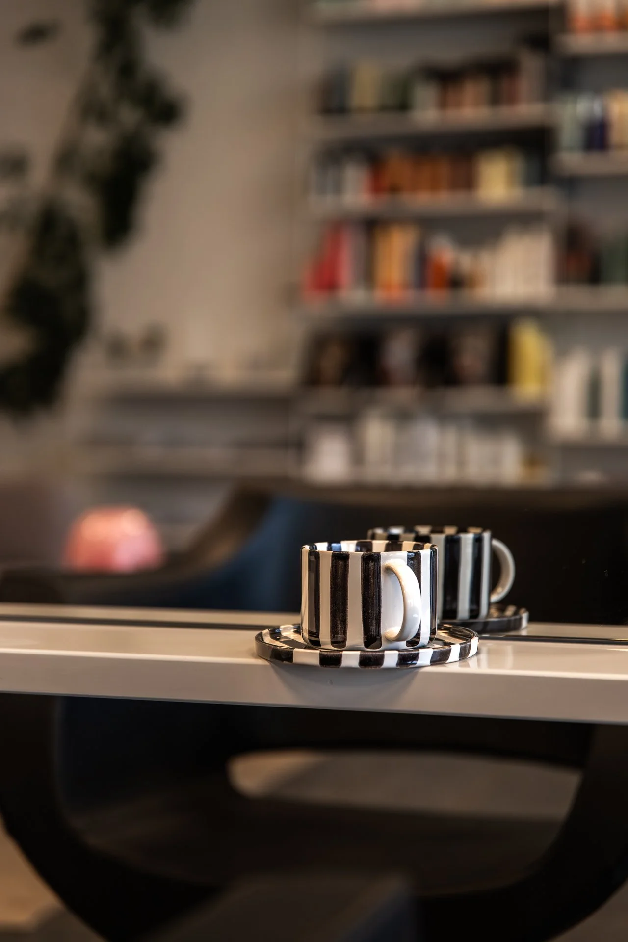 Two coffee mugs with black and white striped pattern on a white surface, with a blurry background of a bookshelf.