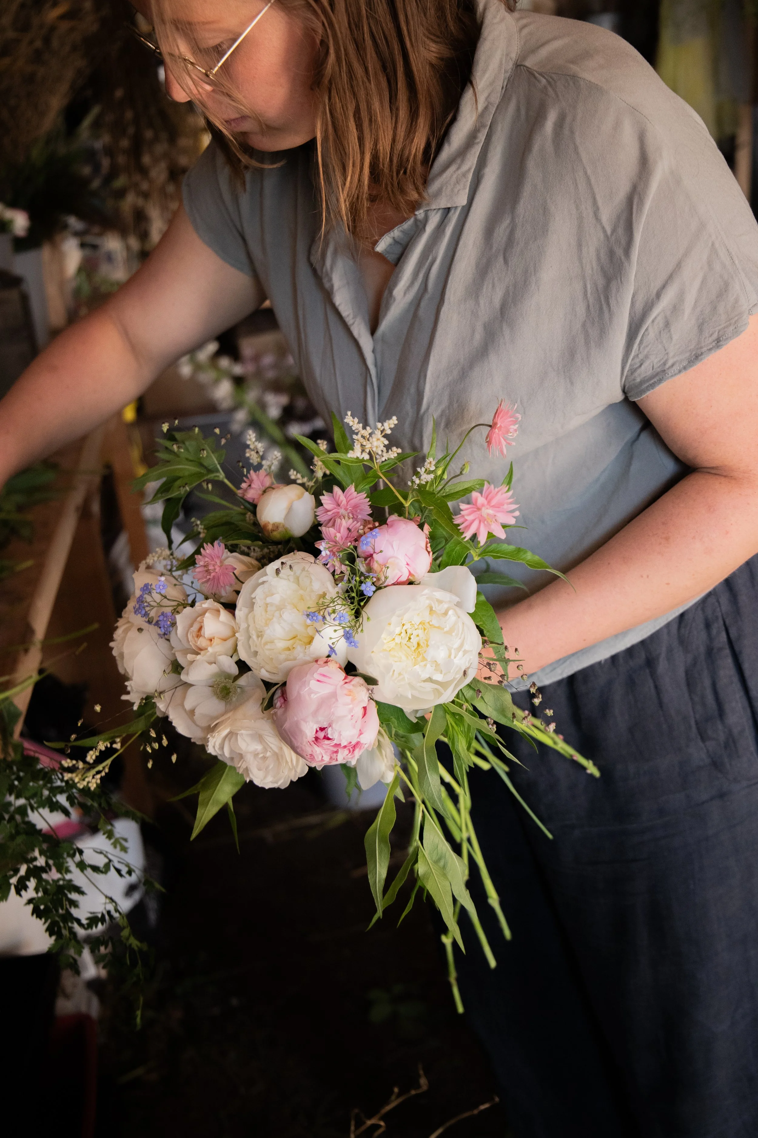 A woman arranging a bouquet of pink, white, and purple flowers in a flower shop.