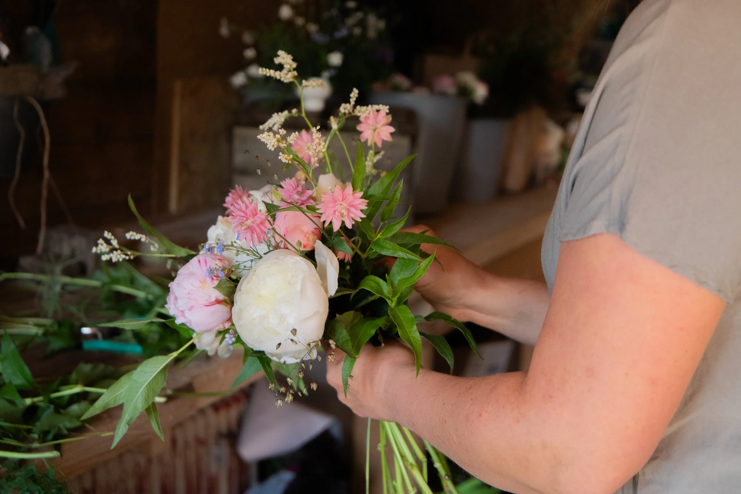 Person holding a bouquet of pink and white flowers in a floral shop.
