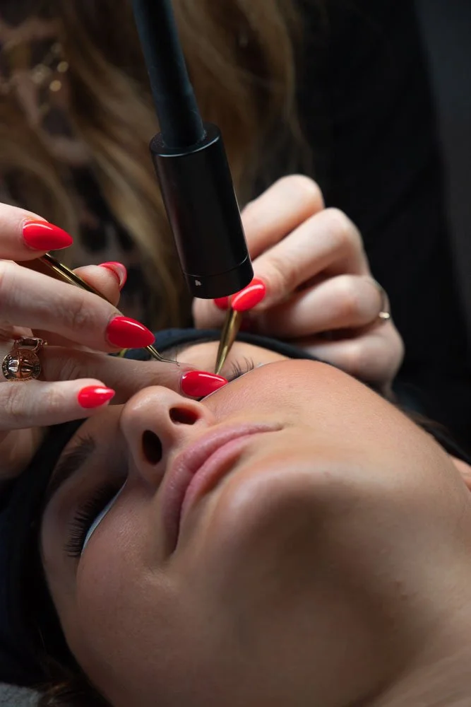 A woman receiving a cosmetic facial treatment with a device on her nose, while lying down with her eyes closed.