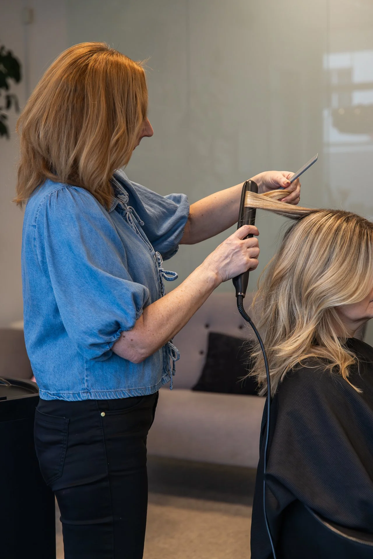 A hairstylist cutting a woman's blonde hair in a salon.