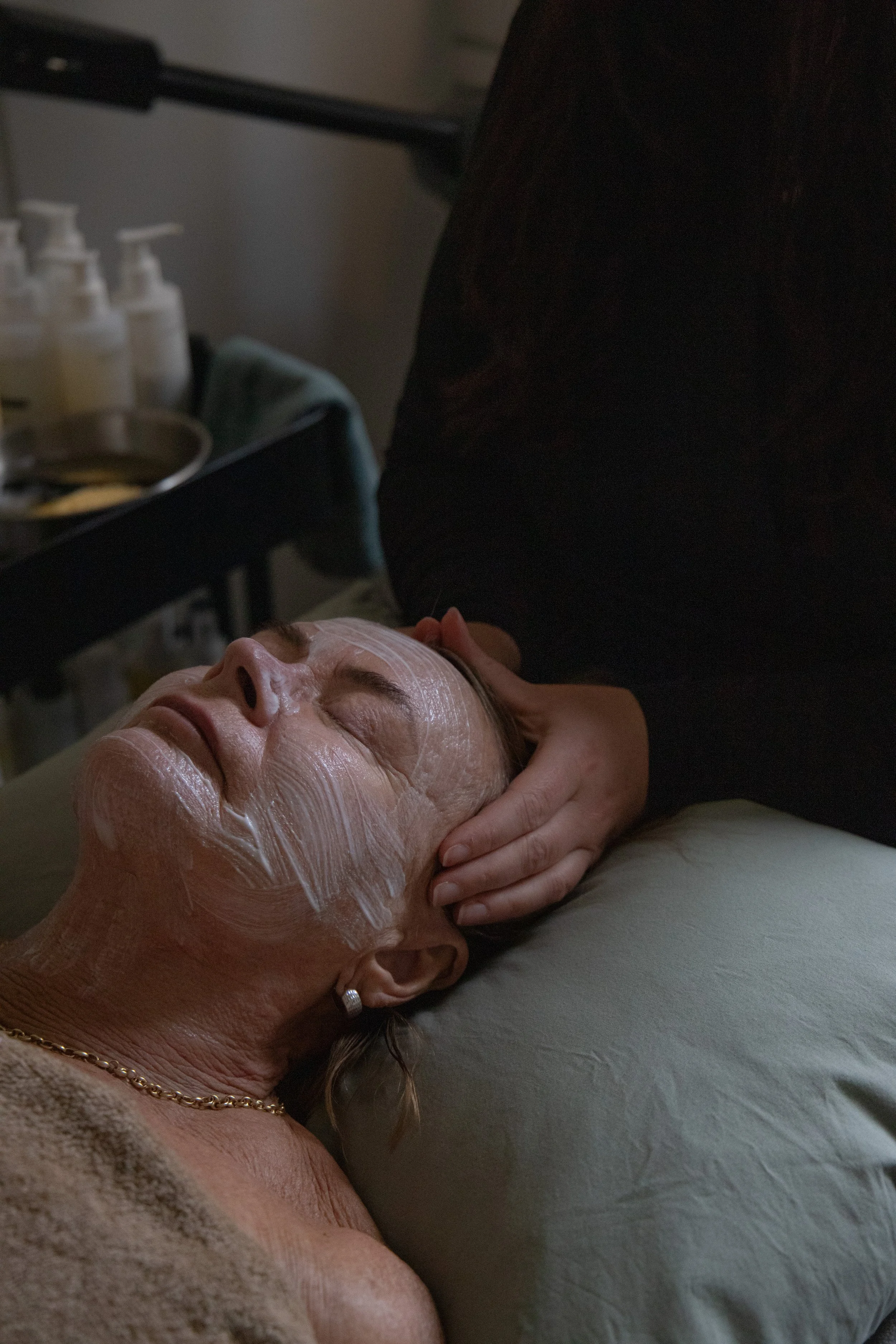 A woman lying on her back with her eyes closed, receiving a facial massage in a spa or skincare setting.