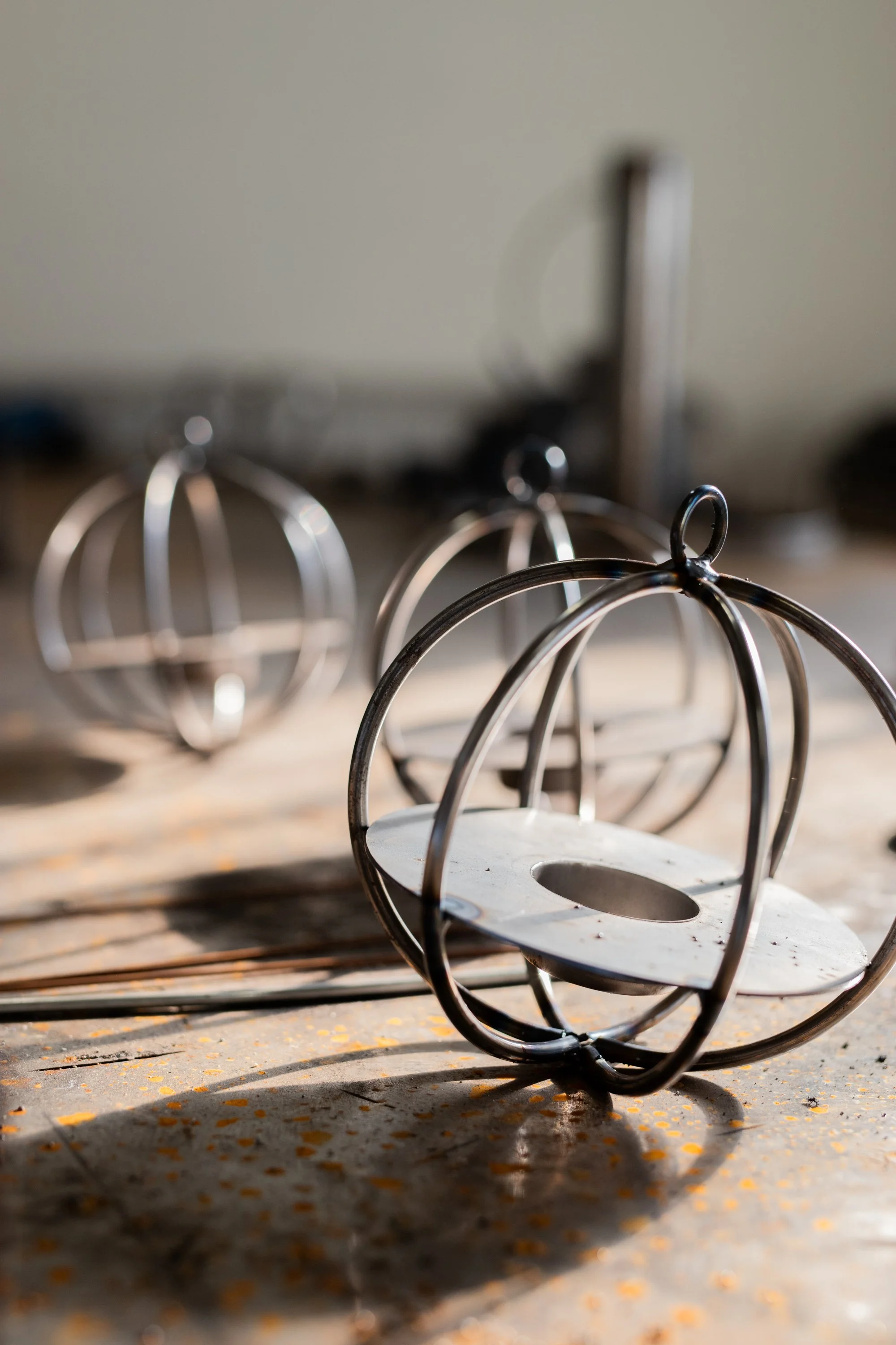 Metal cage-like objects on a wooden surface with sunlight casting shadows, with a blurred background.