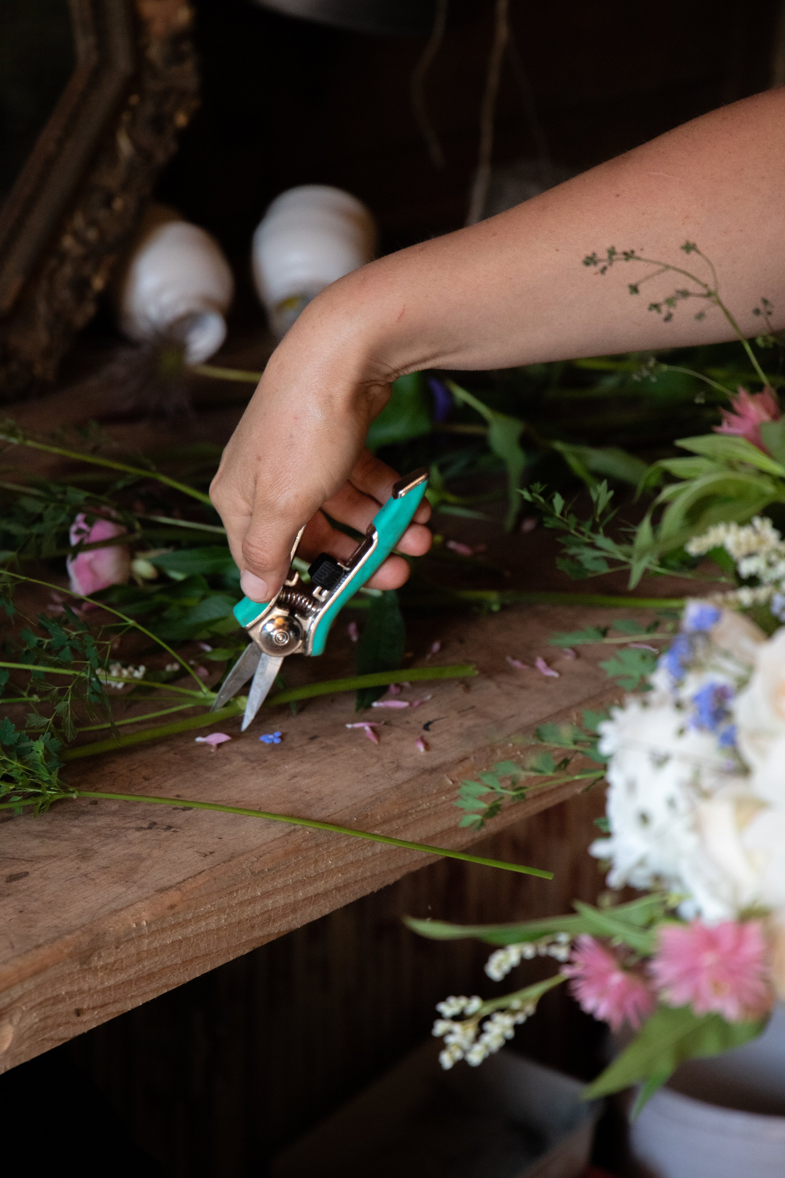 A person trimming a bouquet of flowers with scissors on a wooden table.