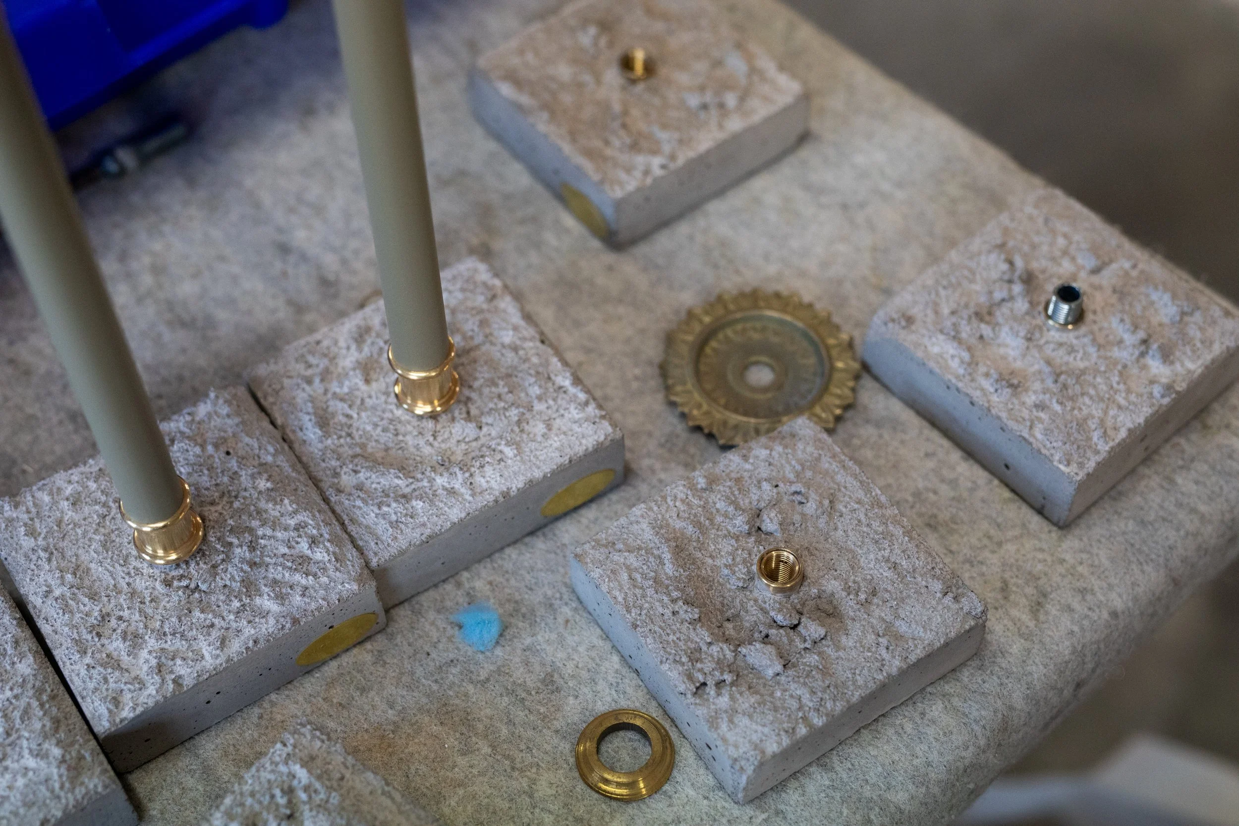 Disassembled furniture or machine parts with metal fittings on stone blocks, including poles, washers, and threaded components, set on a concrete or stone surface.