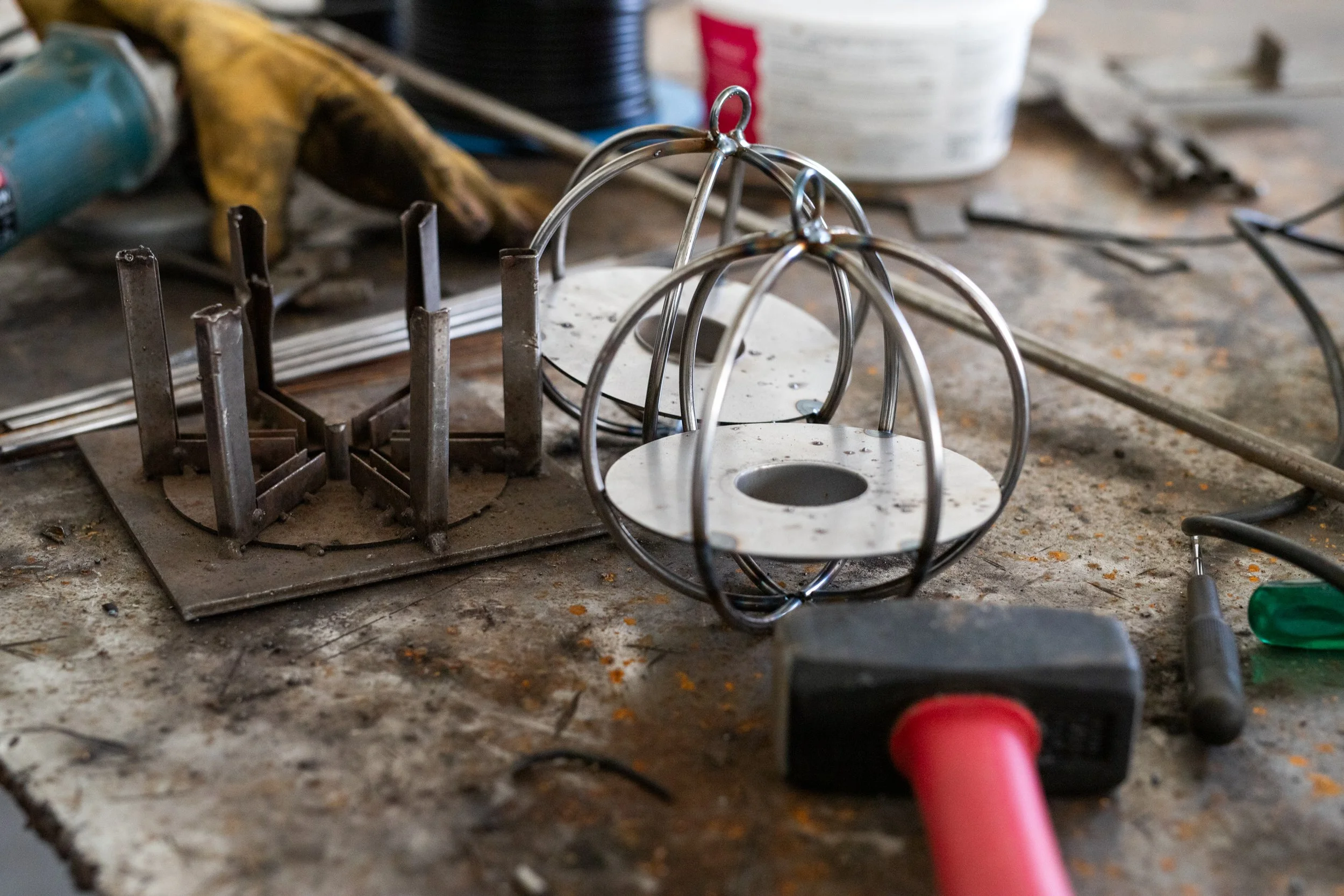 Metal and glass lanterns, tools, and metalwork pieces on a workshop workbench.