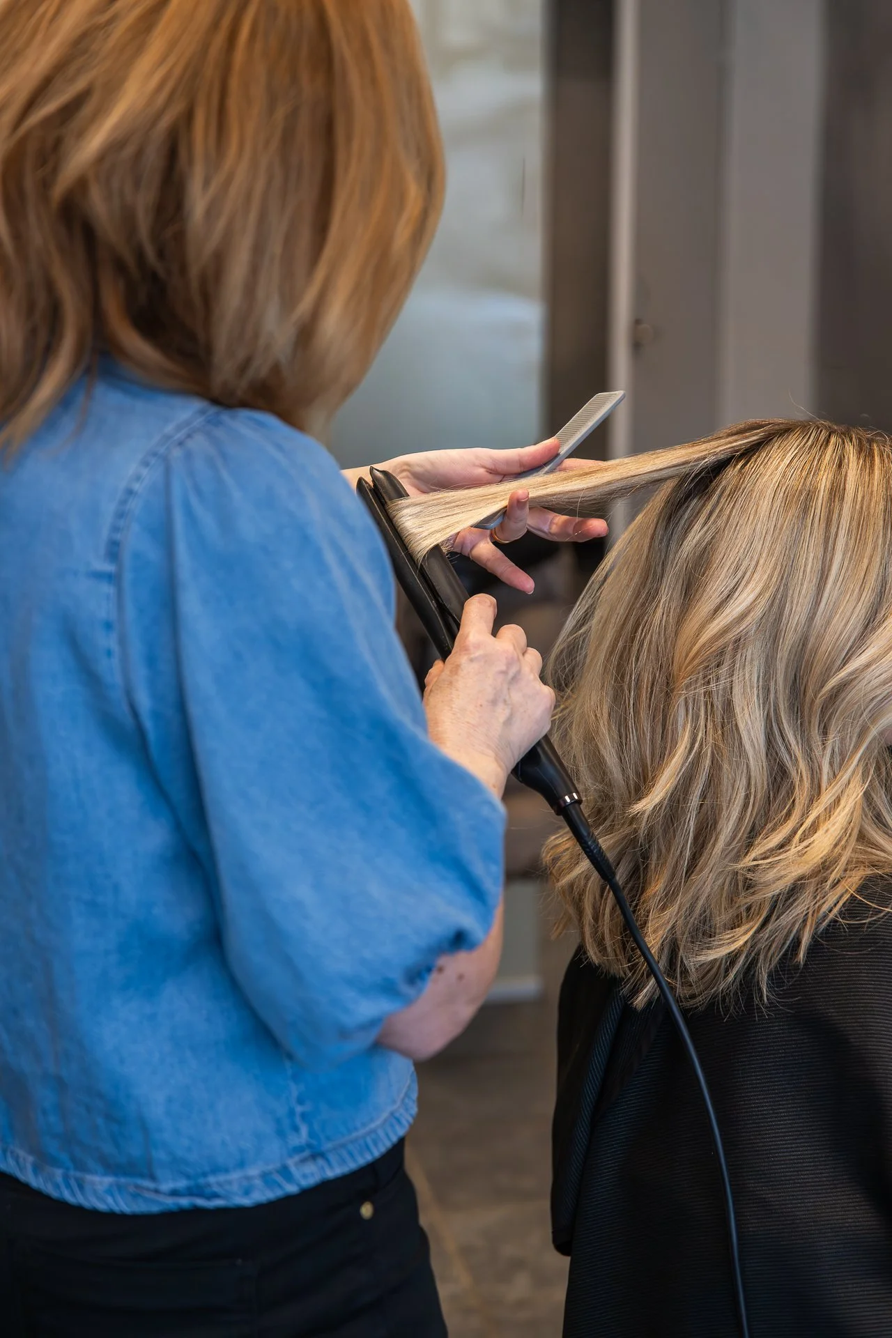A hairdresser drying a woman's hair with a blow dryer and holding a comb.