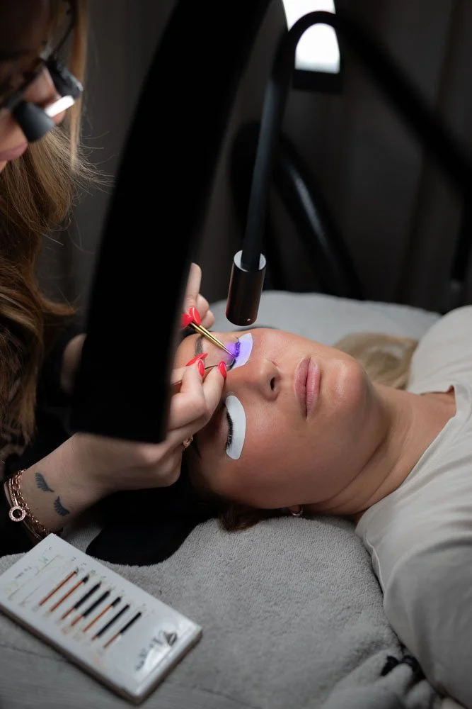 A woman lies on a bed with protective eye patches receiving a laser eye treatment from a technician in a clinical setting.