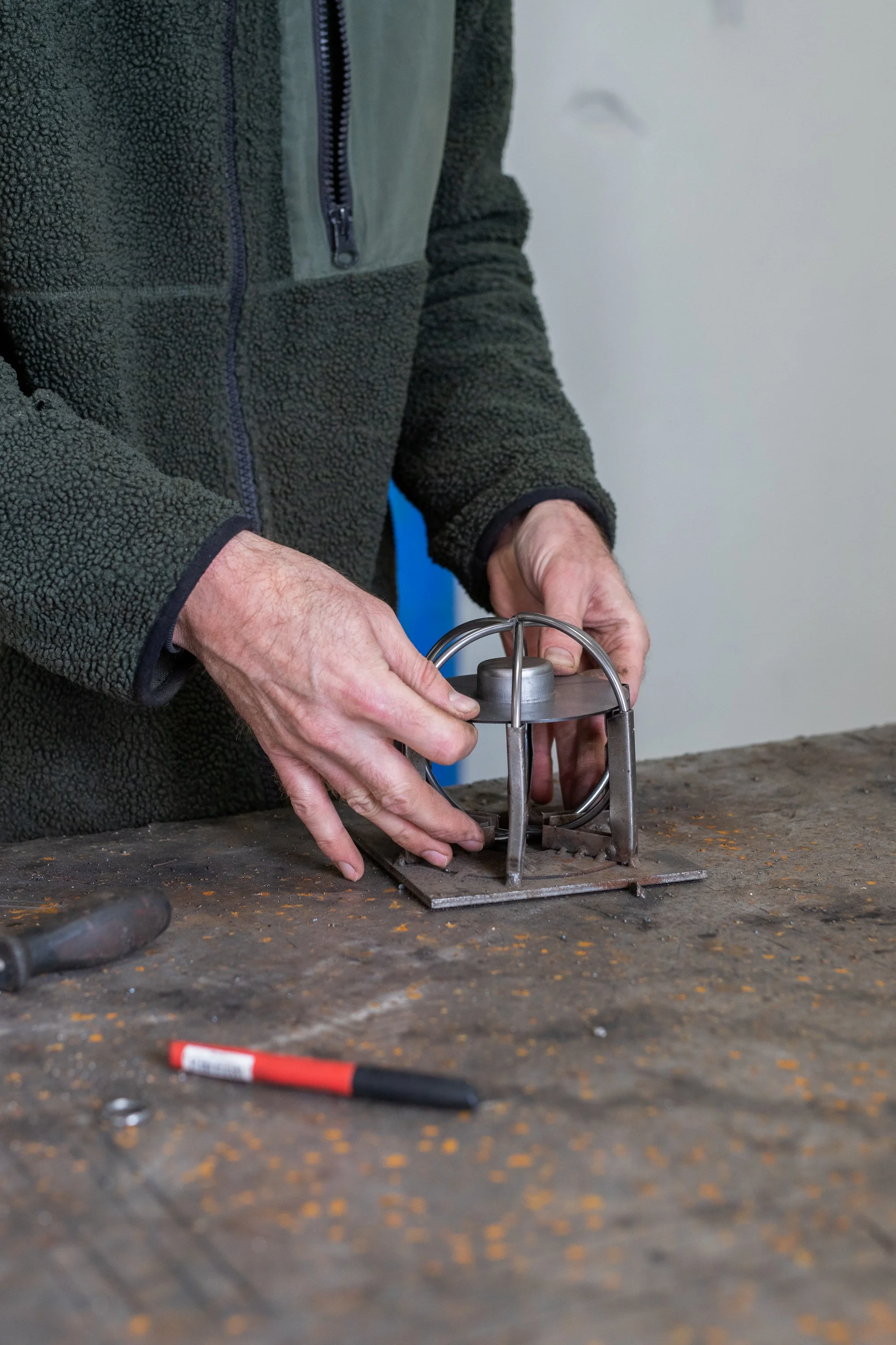 Person working on a metal object using a tool, with a marker pen on a workbench.