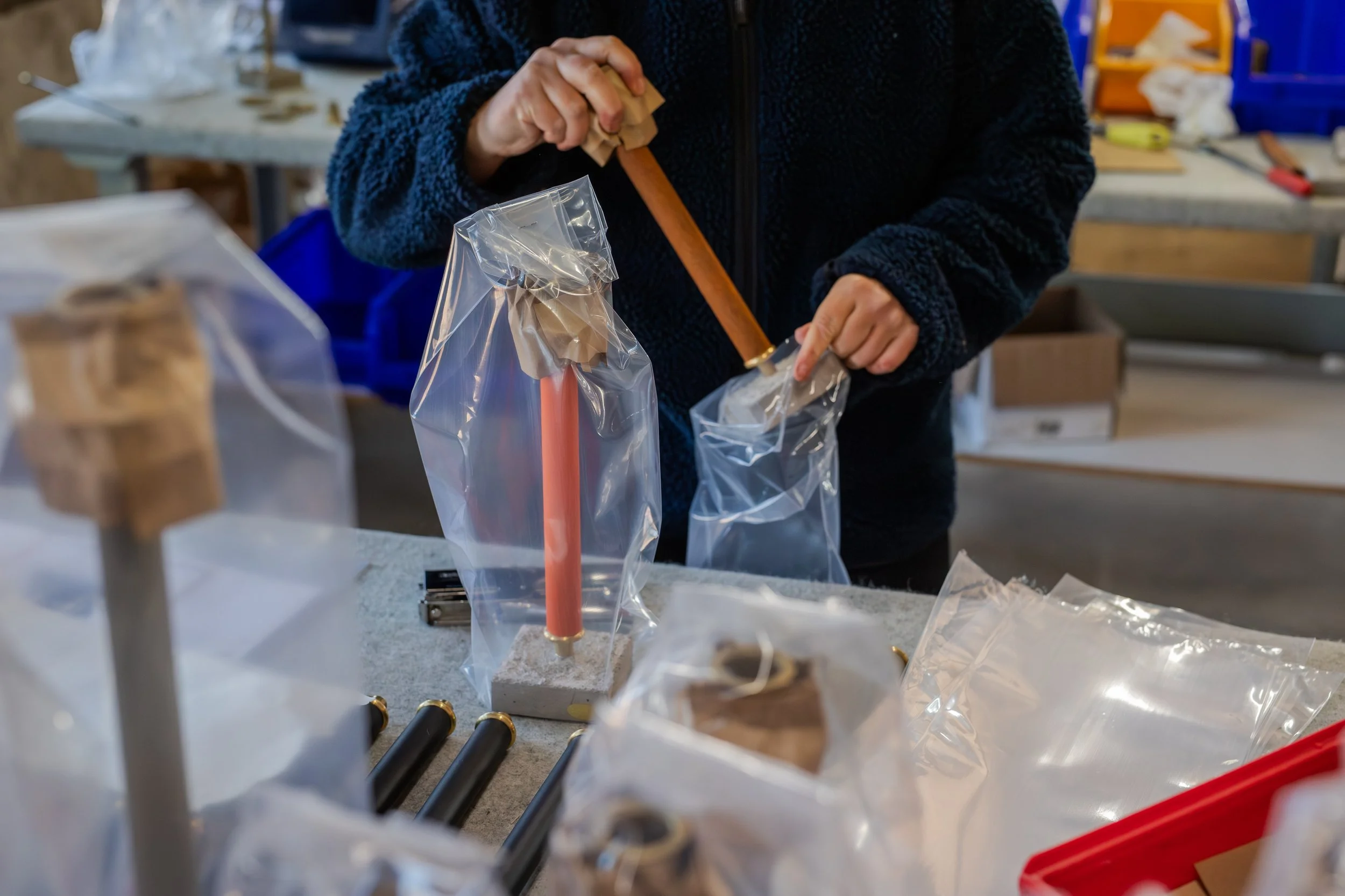 Person working at a workspace, packing items into clear plastic bags with tools and packaging materials around.
