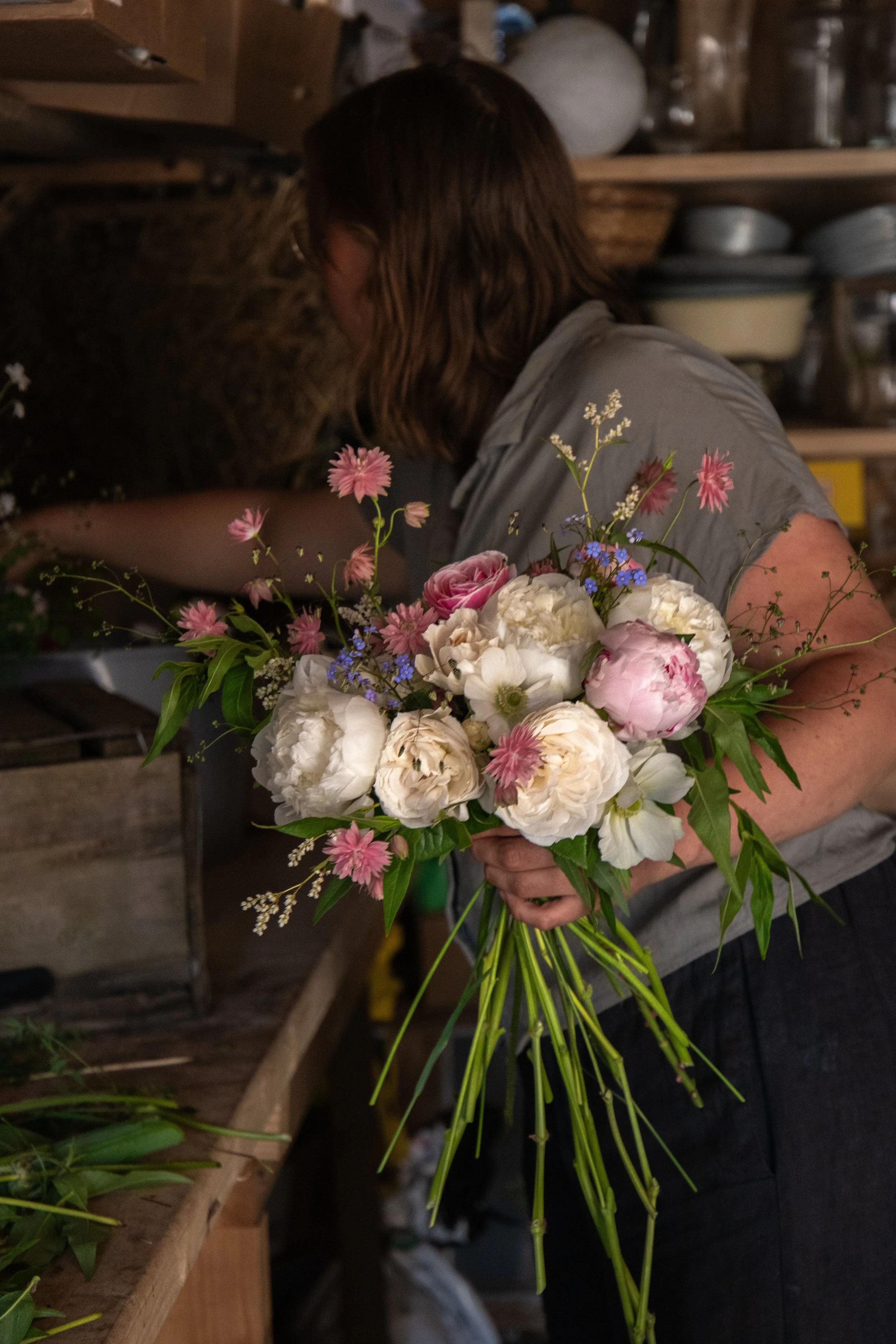 A person arranging flowers in a workshop, holding a bouquet of pink and white flowers with greenery.