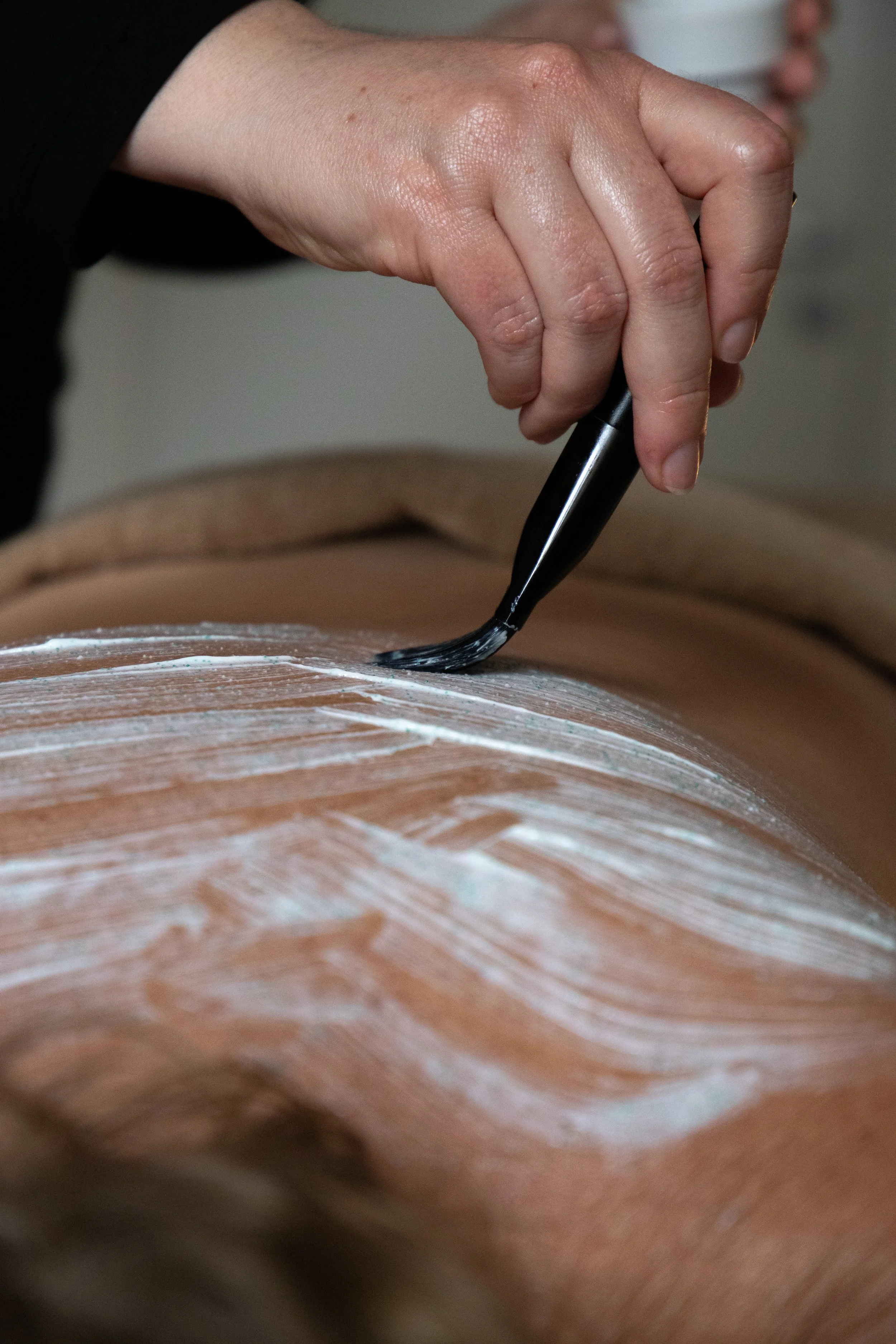 A person receiving a back massage with oil and a massage brush applied to their back.