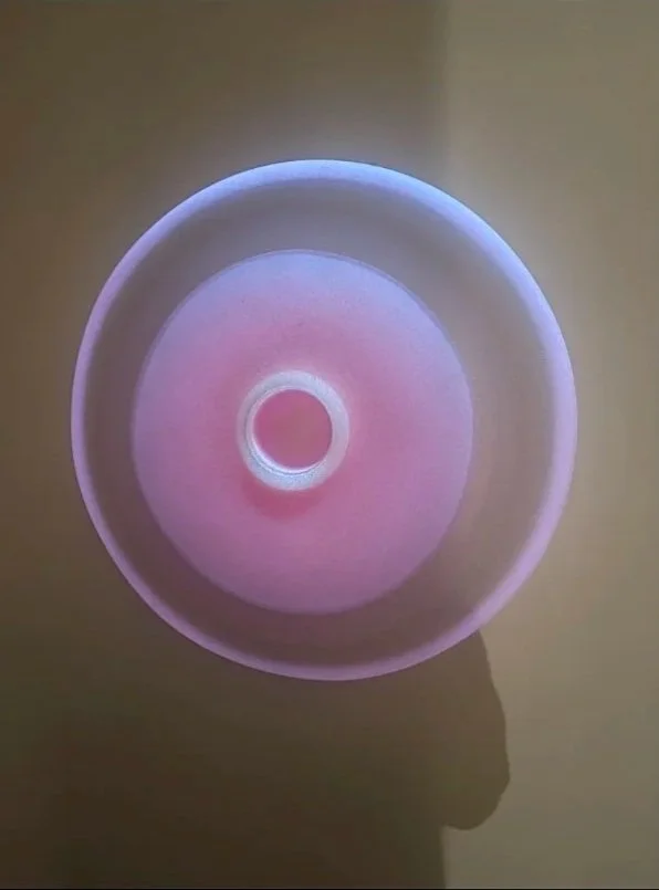 View of a circular, glowing, multicolored light or display with shades of pink and purple on a beige background.