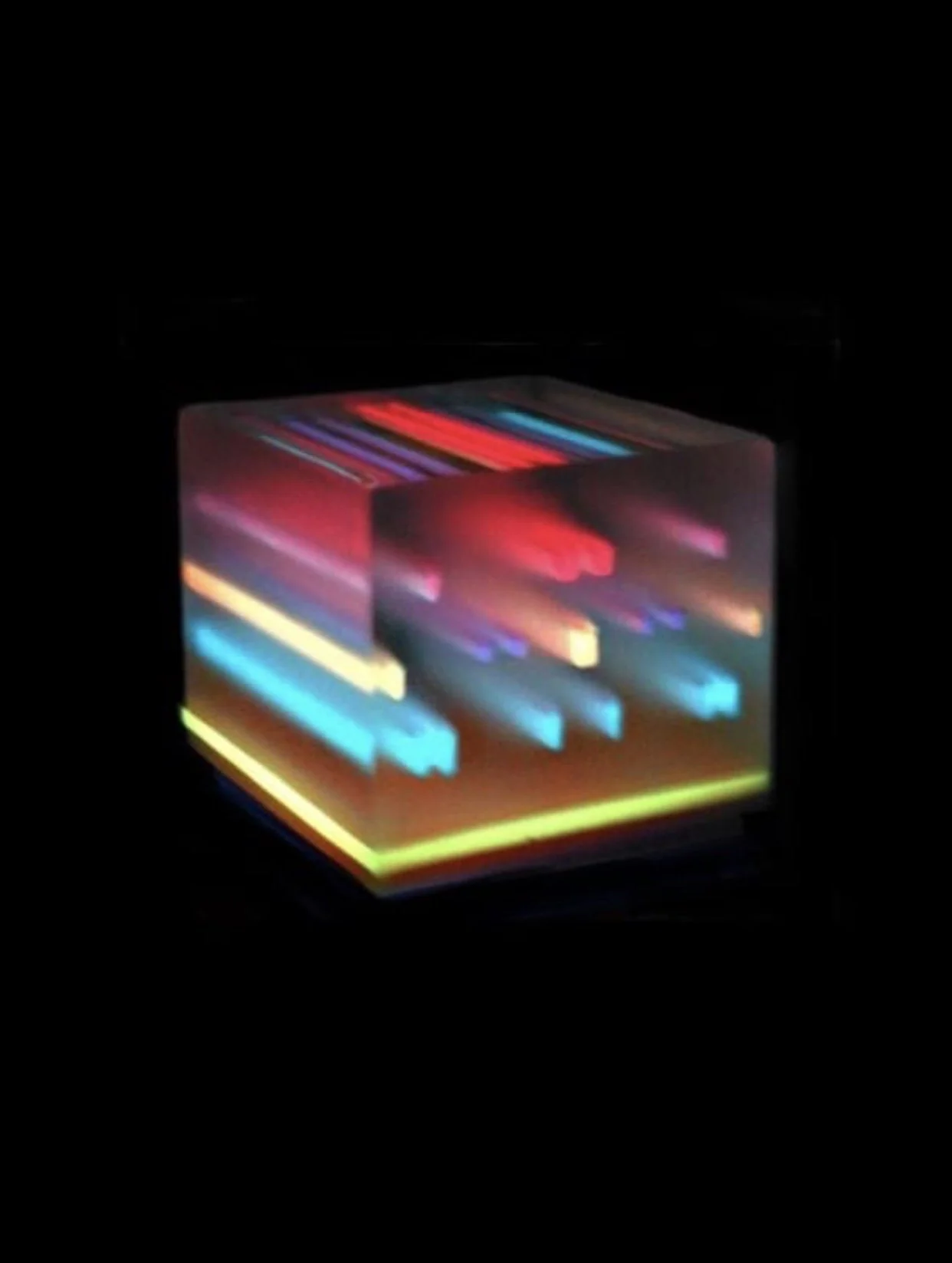 A small cube with colorful glowing lines and patterns on its sides, lit up in a dark environment.