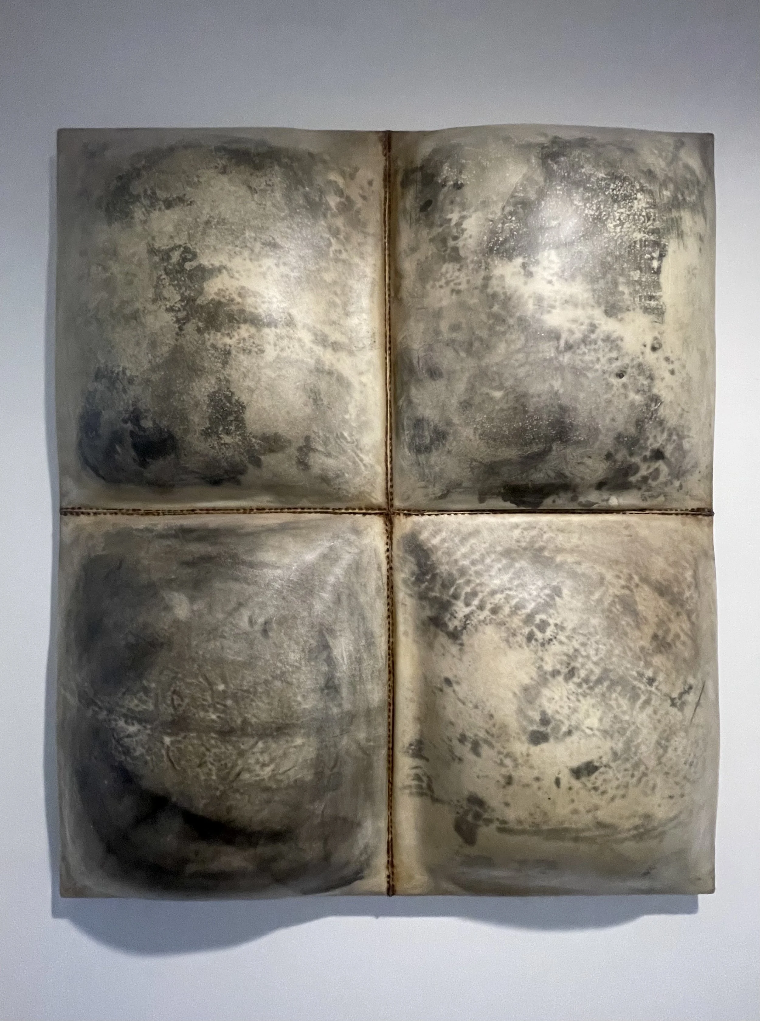 A square sculpture made of four ceramic tiles with a textured, abstract pattern resembling weathered stone, arranged in a 2x2 grid with a small gap between them.