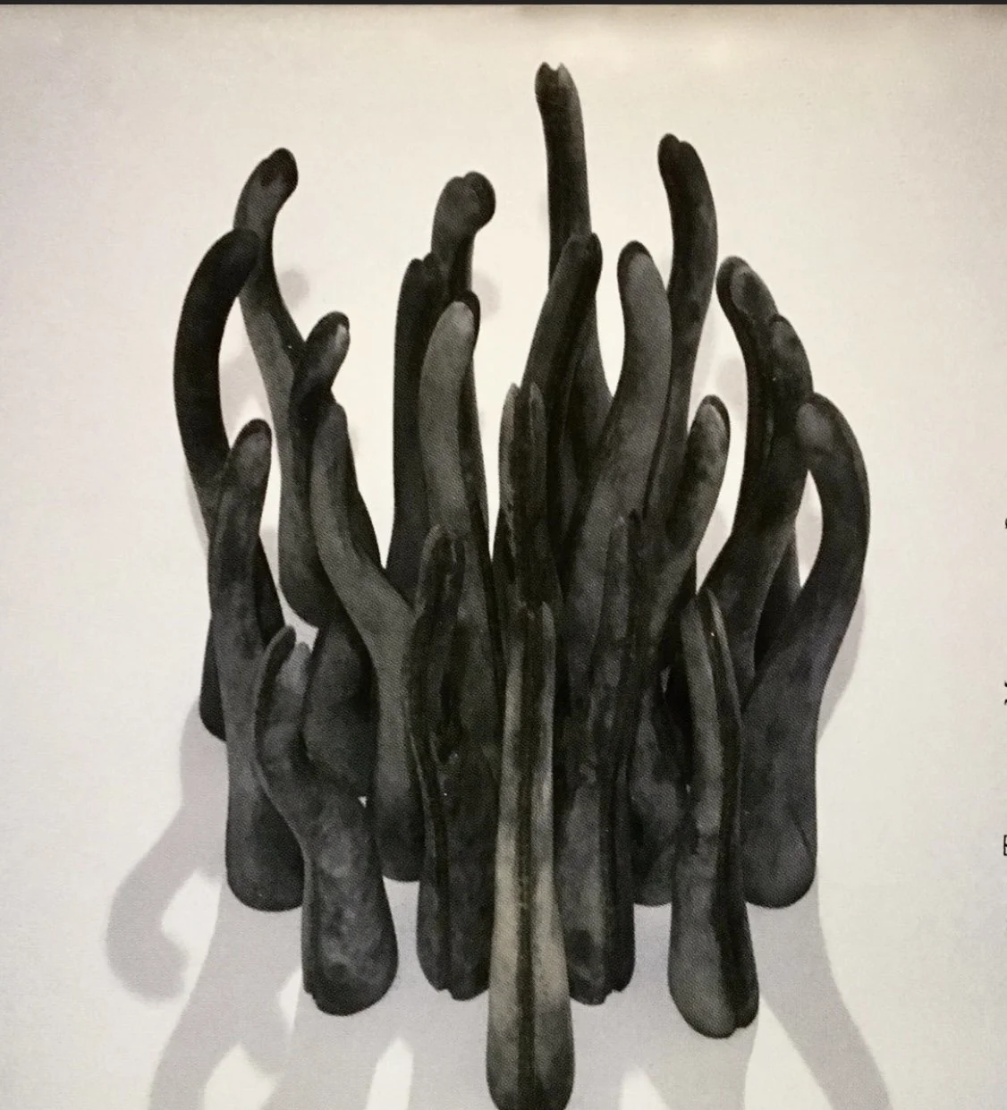 Sculpture of multiple black intertwined hands with elongated fingers, arranged in a clustered formation against a plain background.