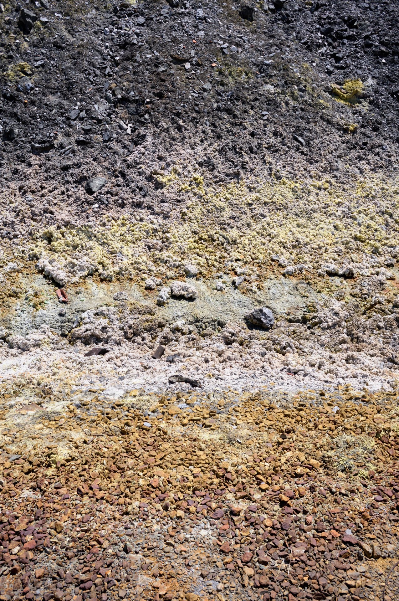 Multiple layers of different colored soil and rocks, ranging from dark blackish soil at the top to reddish rocks at the bottom.