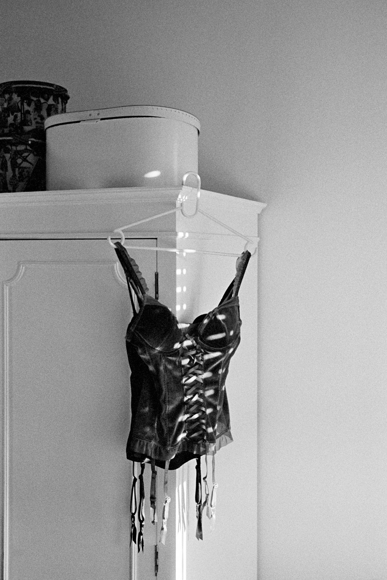 Black leather harness with hanging straps, hanging from a white wall hook in a room with a white cabinet and a decorative object on top.