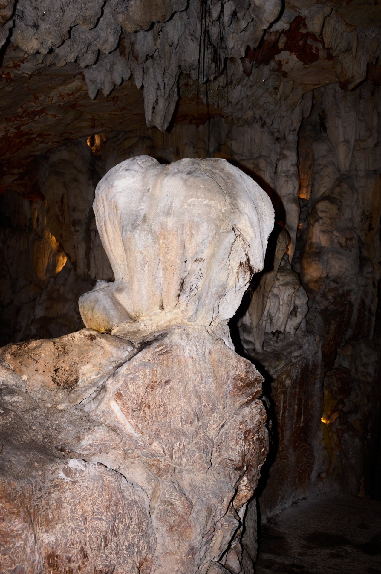 Inside of a cave with large rocks and stalactites, showing a white rock formation prominently in the center.