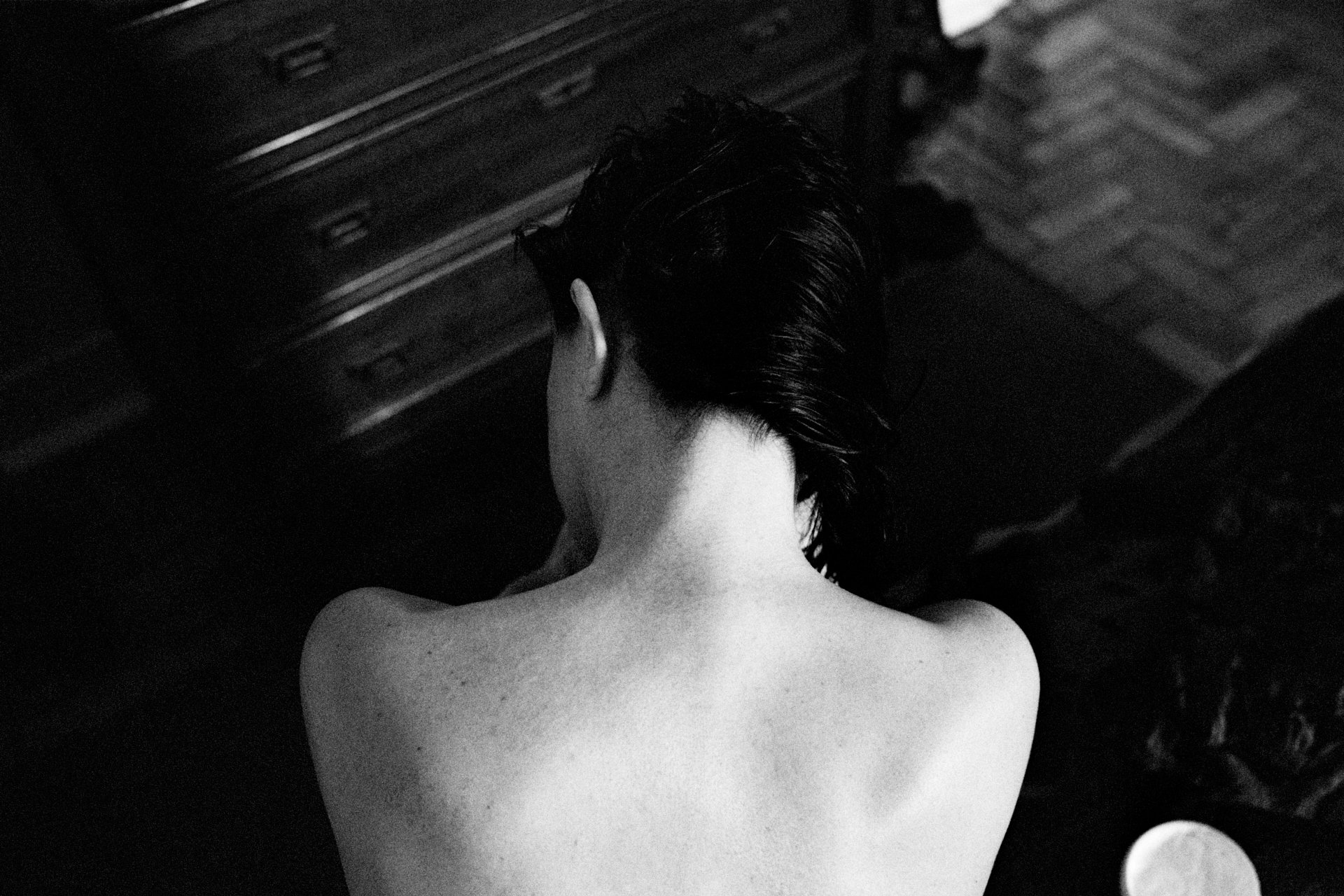 Black and white photo of a person's back with short, wavy hair, sitting on a dark surface.