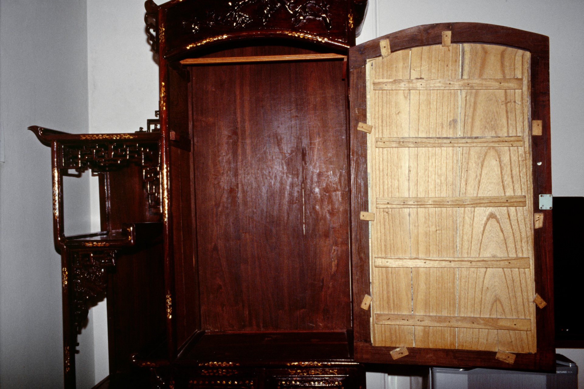 The image shows the underside of a wooden bed frame or headboard, with a detailed and ornate dark-colored wood design on the exterior and light-colored slats on the interior, supported by small wooden blocks.