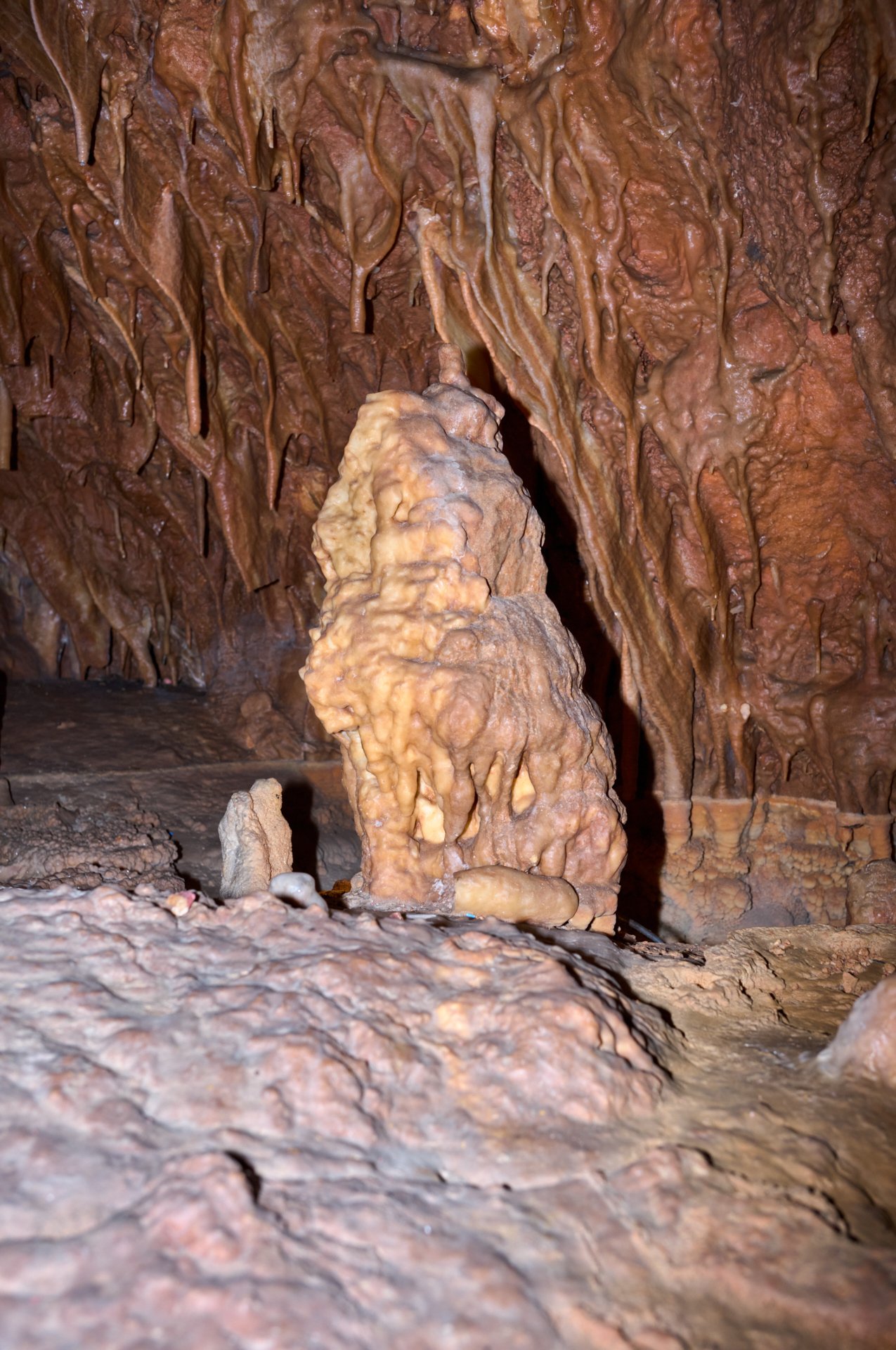 View of a cave with stalactites hanging from the ceiling and a stalagmite on the ground, both formed from mineral deposits.