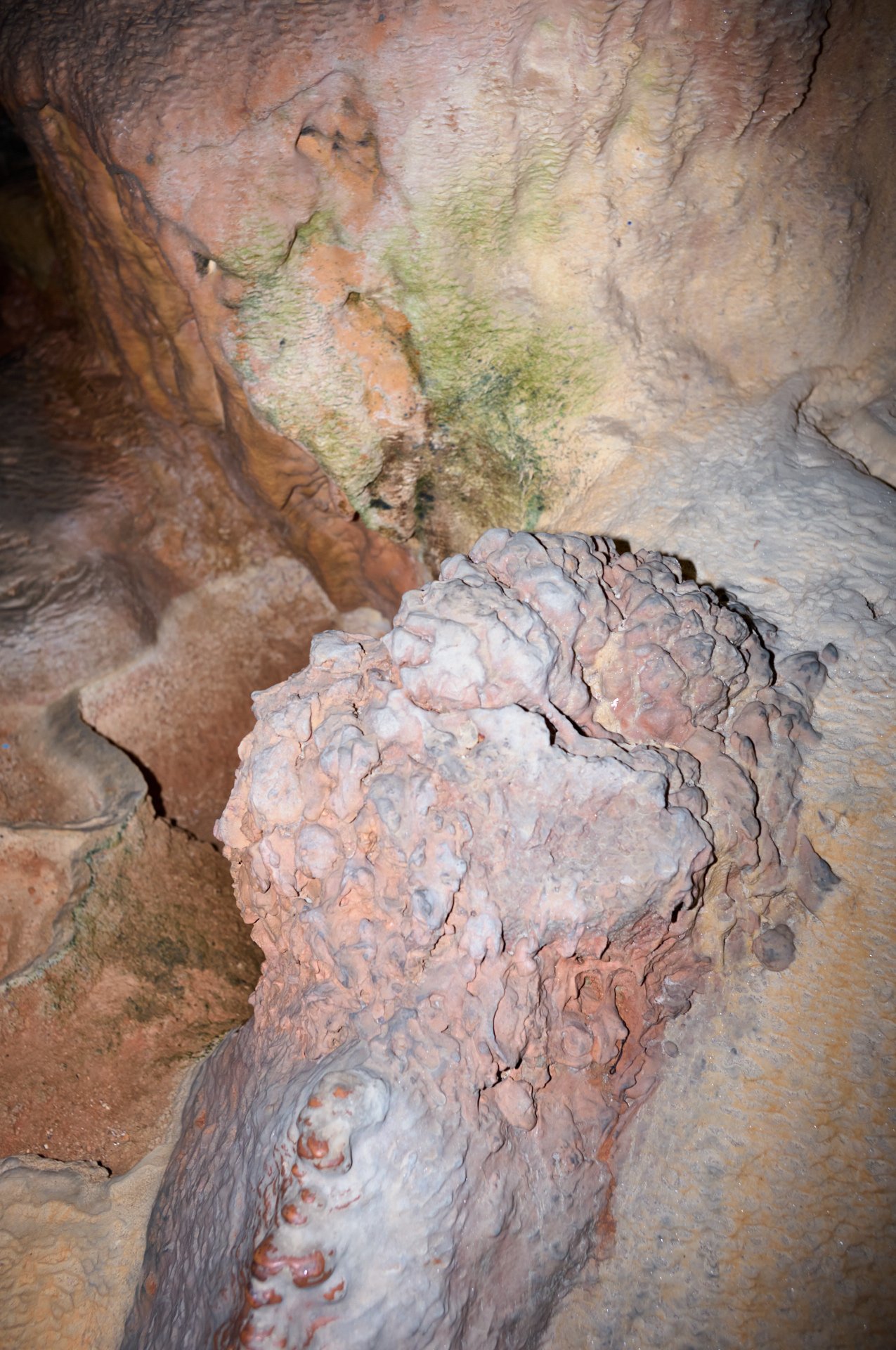 Close-up of a large, irregular rock formation inside a cave, with some green moss or algae growth visible on the surface.