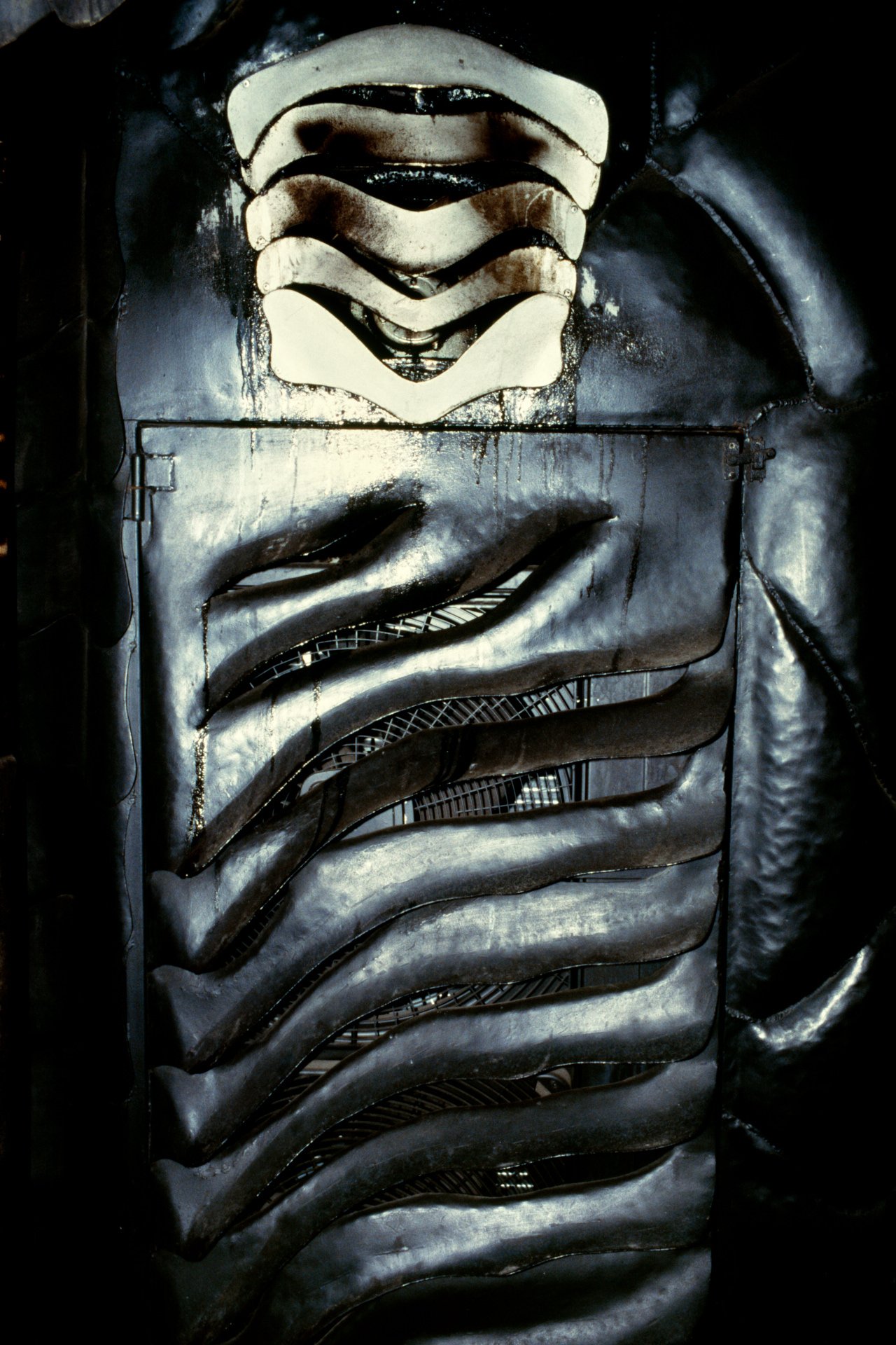 Metal sculpture featuring abstract, organic shapes with layered, curved elements in a dark setting.