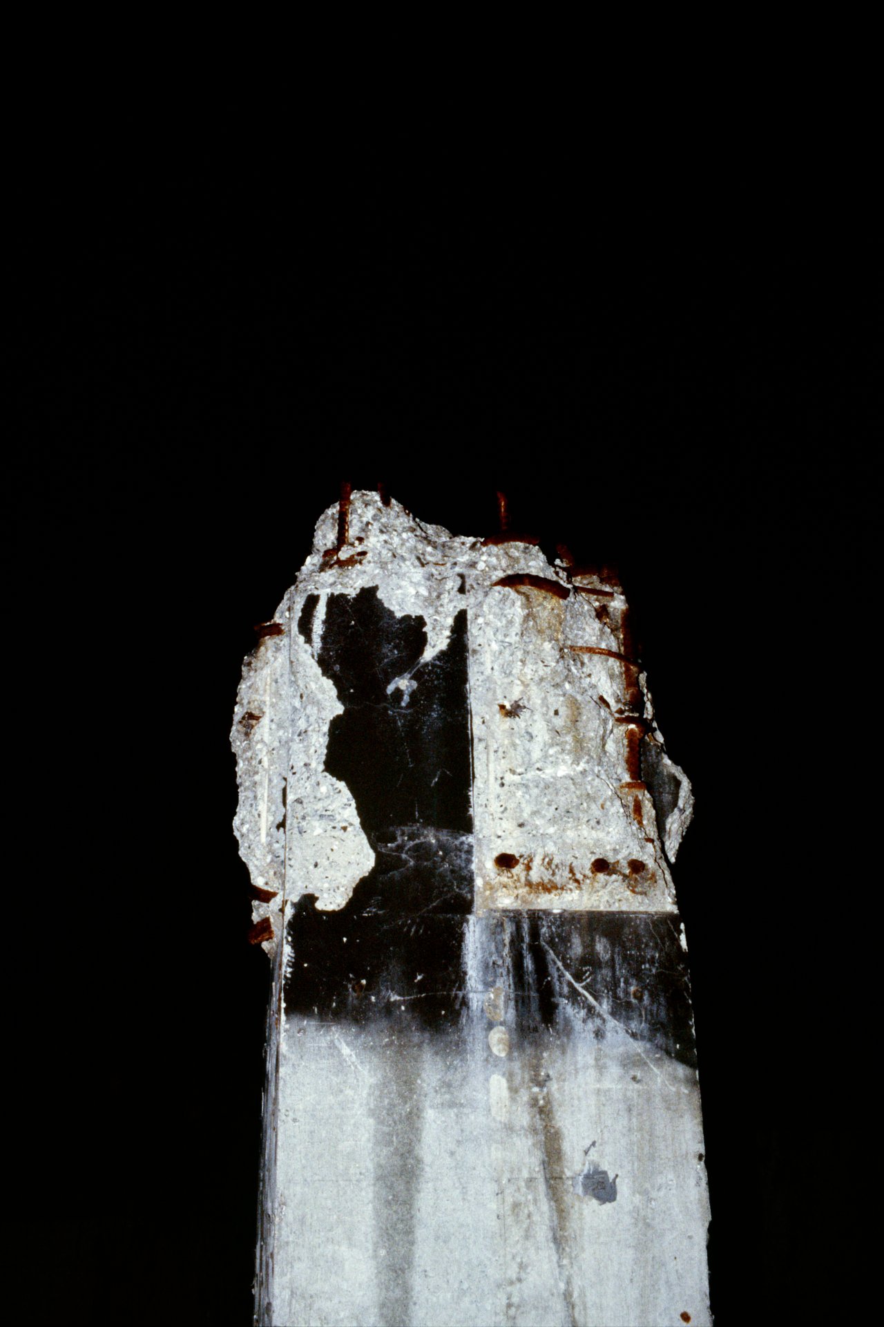 Close-up of a damaged concrete pillar with exposed rebar against a black background.