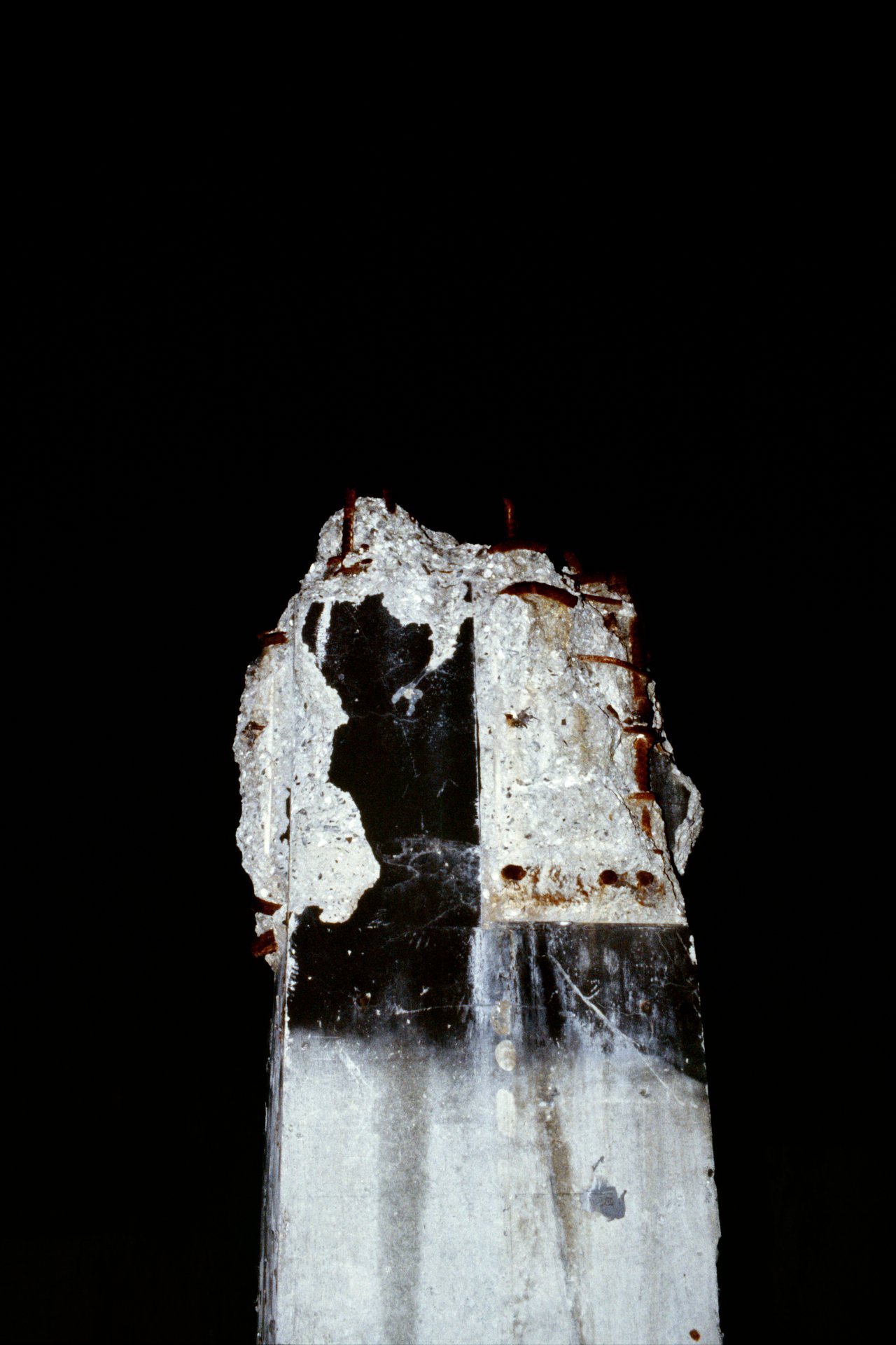 A tall, weathered concrete monument with a black silhouette of a person’s profile on a dark background.
