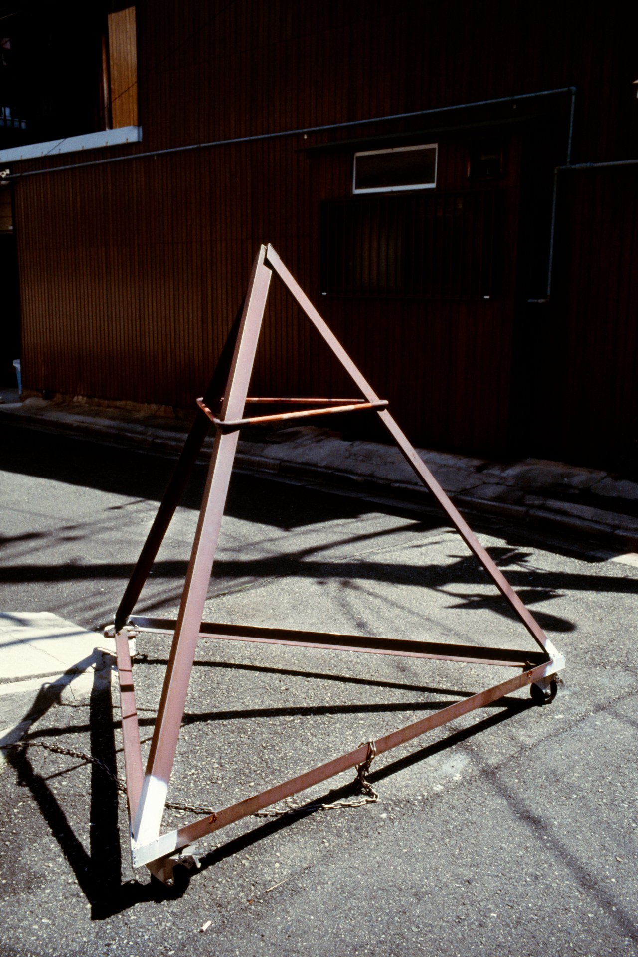 Empty metal A-frame sidewalk sign frame on a city street with shadow.
