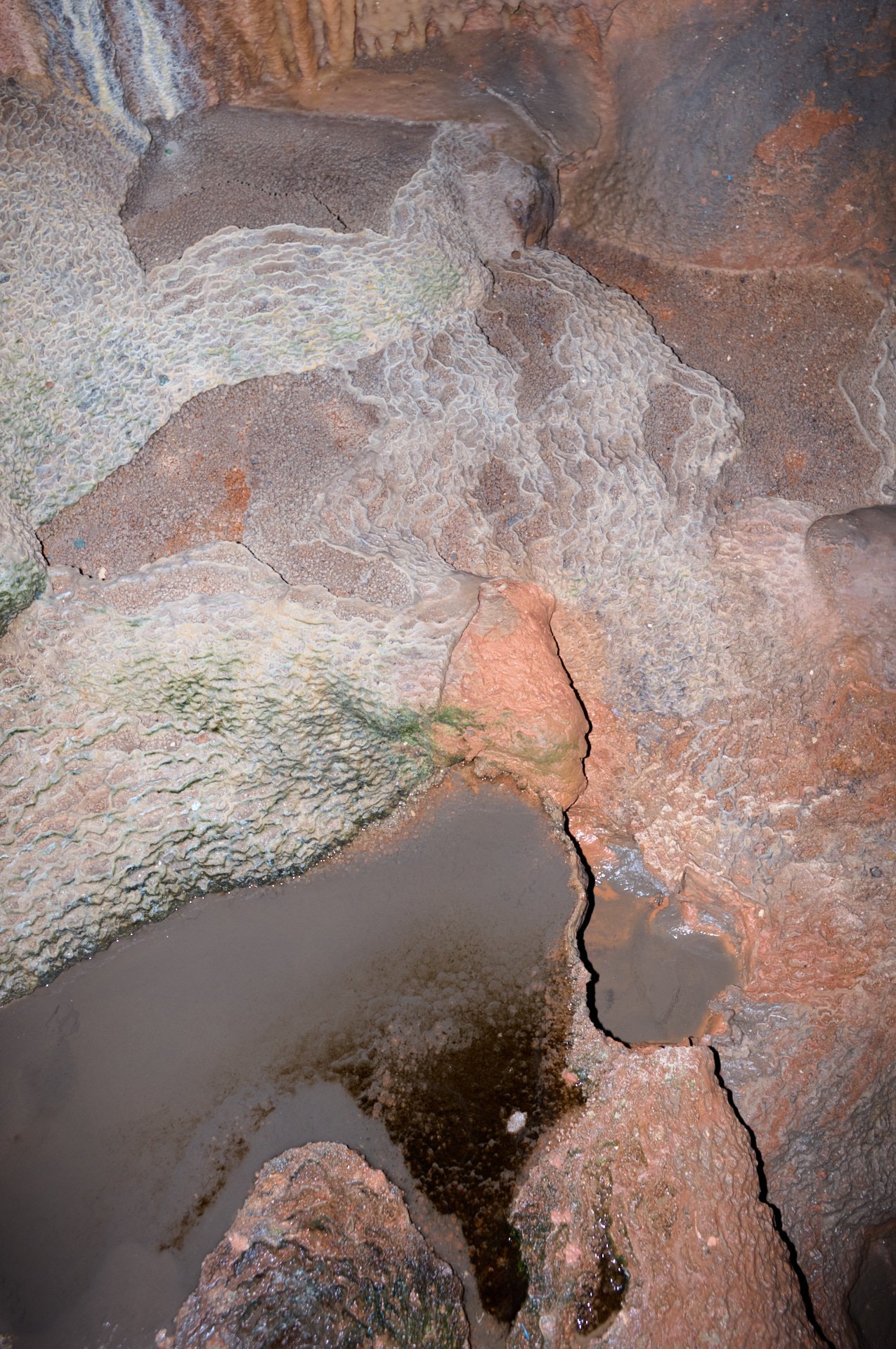 Close-up of mineral-rich rock formations and pools of water inside a cave.