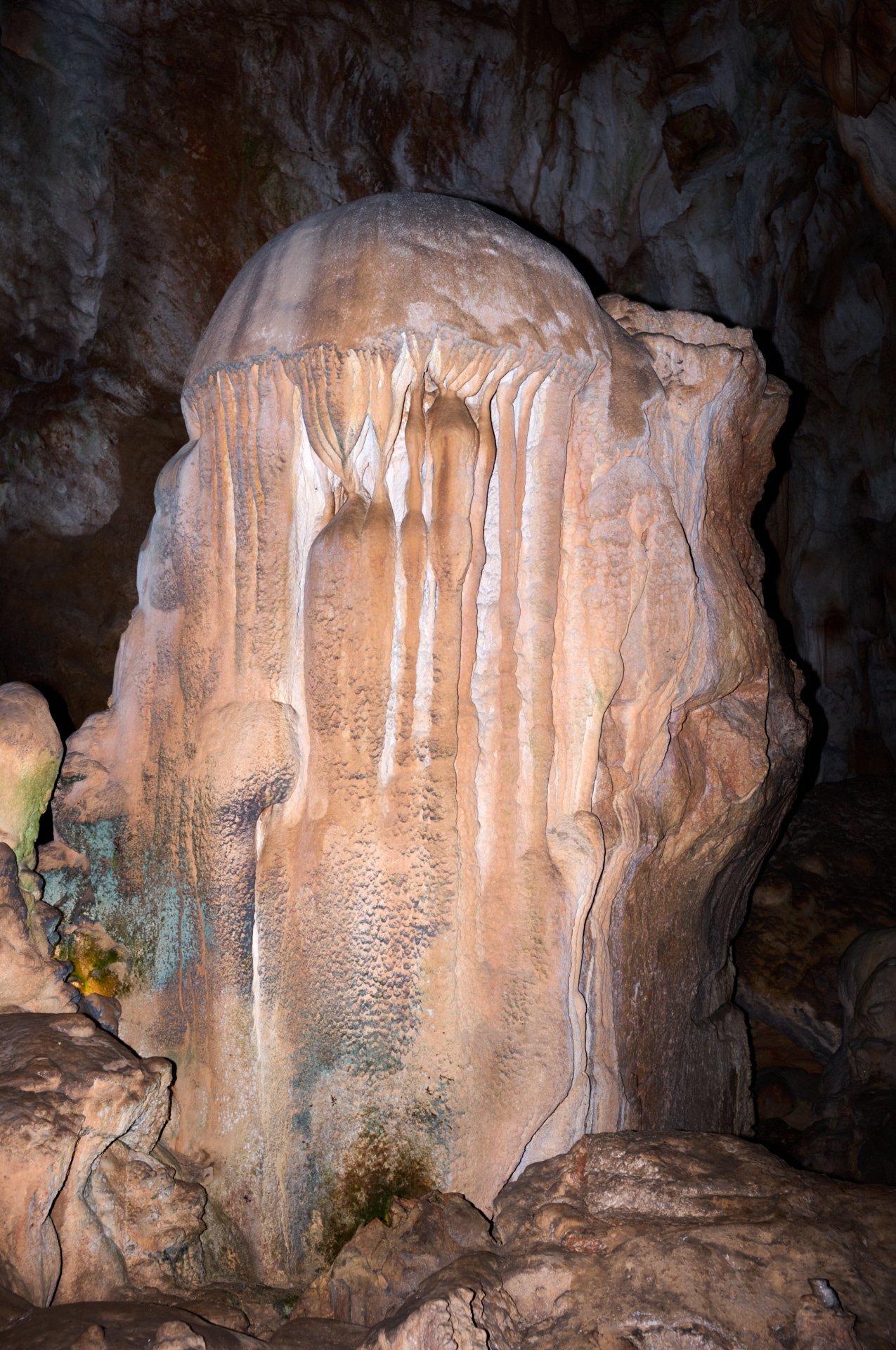 A large cave formation with stalactites and stalagmites, featuring a prominent stalagmite with flowstone deposits on its surface.