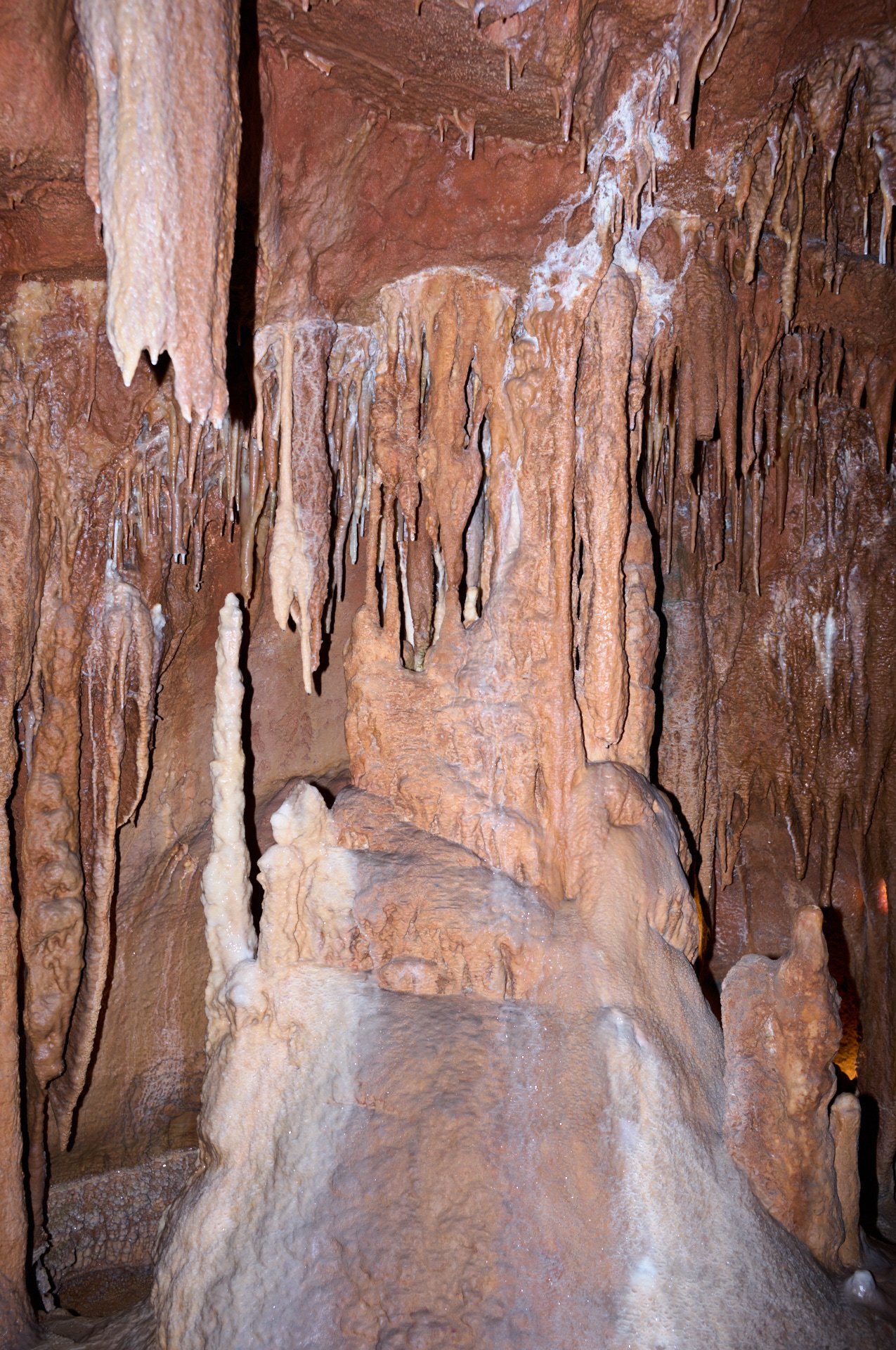 Inside a cave with stalactites hanging from the ceiling and stalagmites rising from the ground, with mineral deposits creating varied textures and formations.