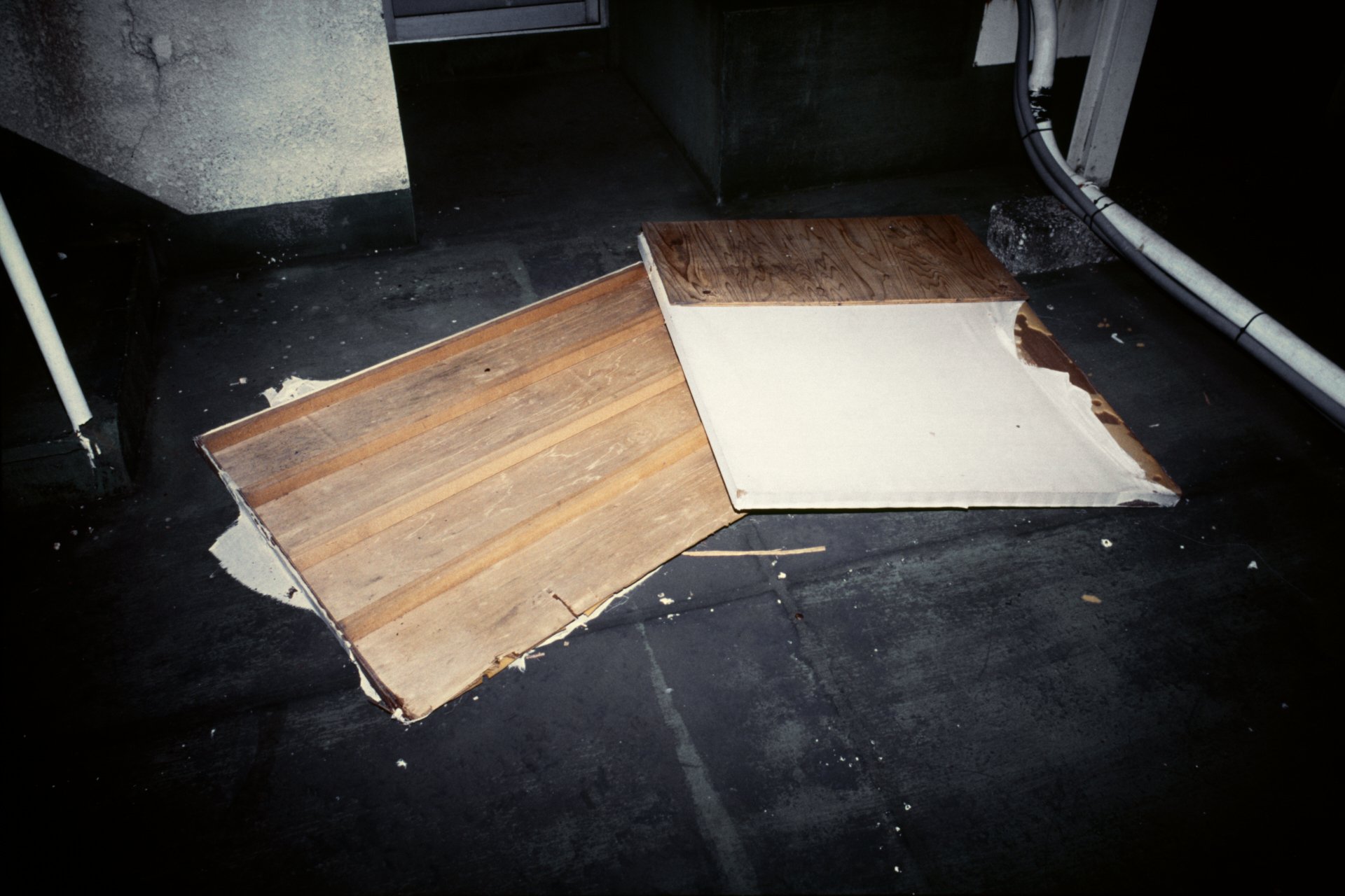Broken wooden floor panel lying on a black surface, with part of it covered in white material in an industrial or construction setting.