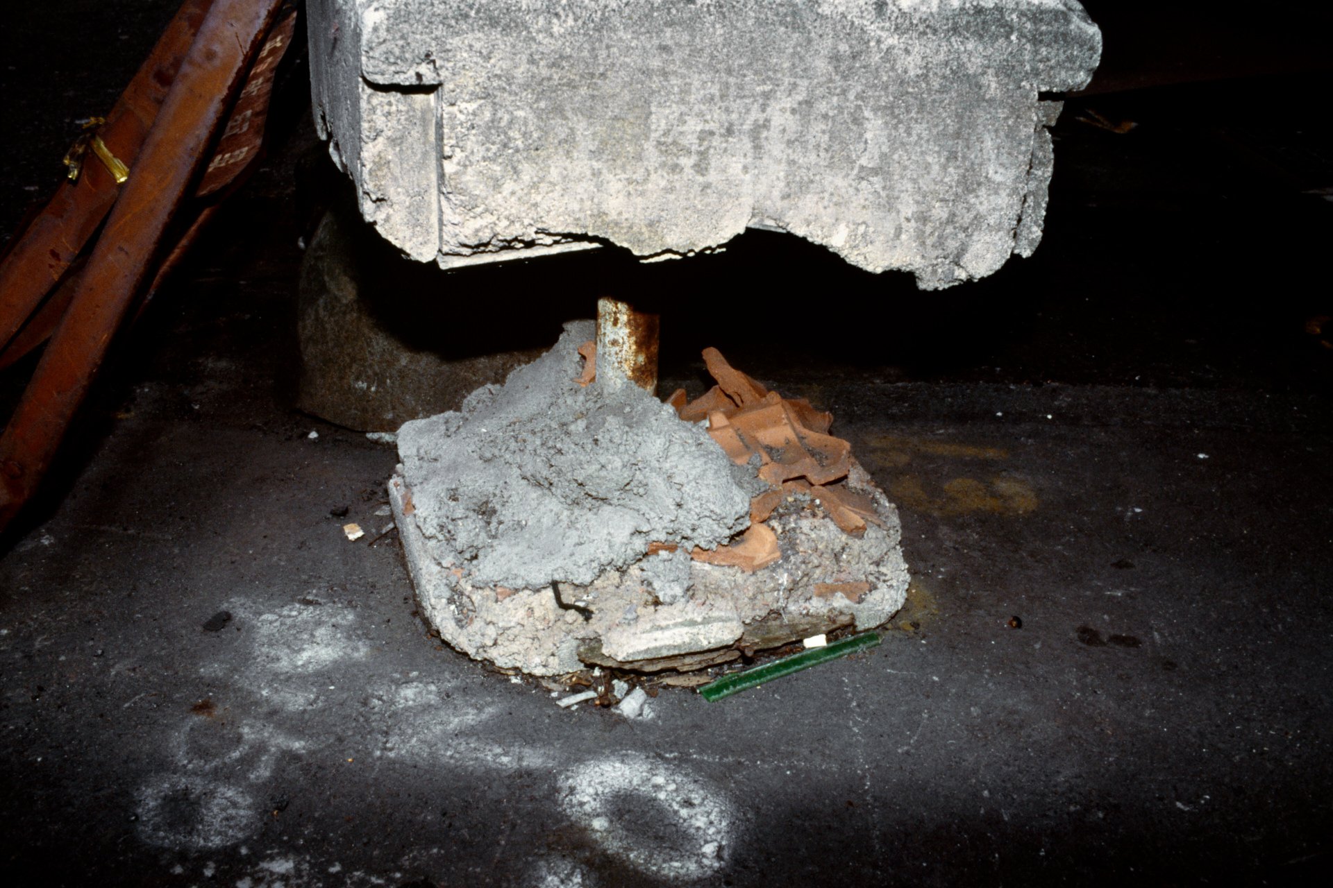 Broken concrete block with debris and rubble underneath, on a dark surface