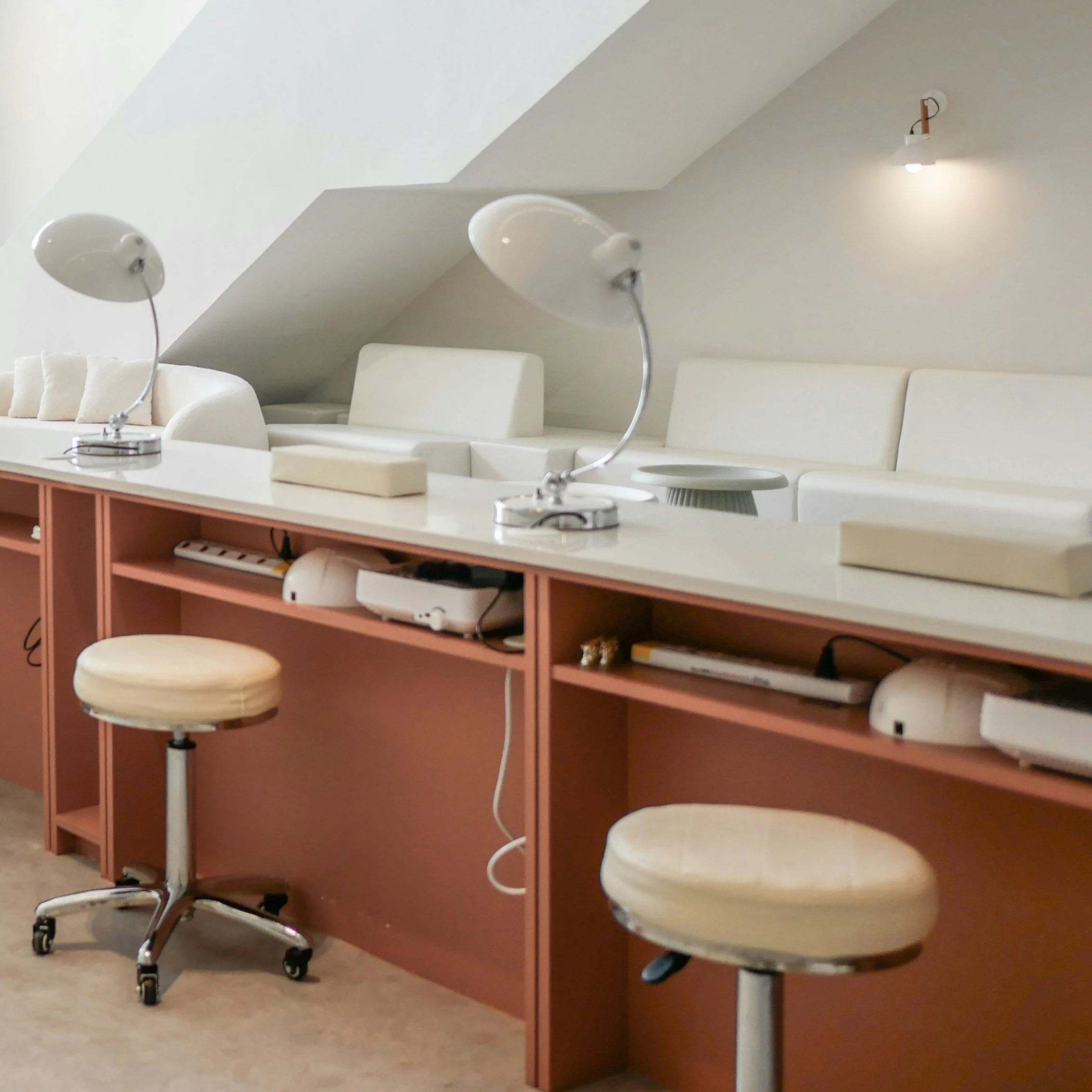 Medical examination room with beige stools, a white counter, and a brown cabinet, with three white lamps hanging from the ceiling and a light fixture on the wall.