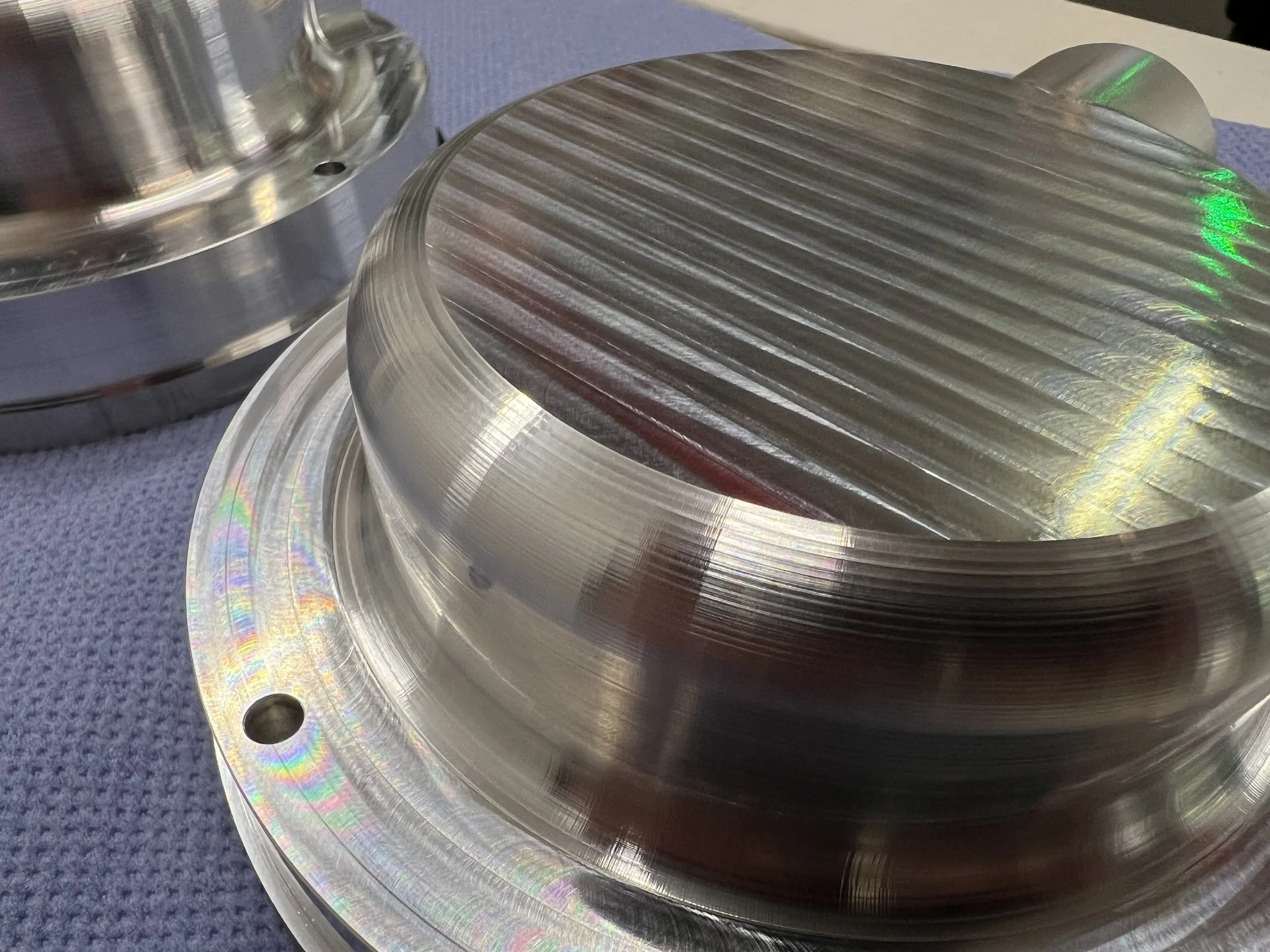 Close-up of polished metal mechanical component with grooved surface, sitting on a blue textured cloth.