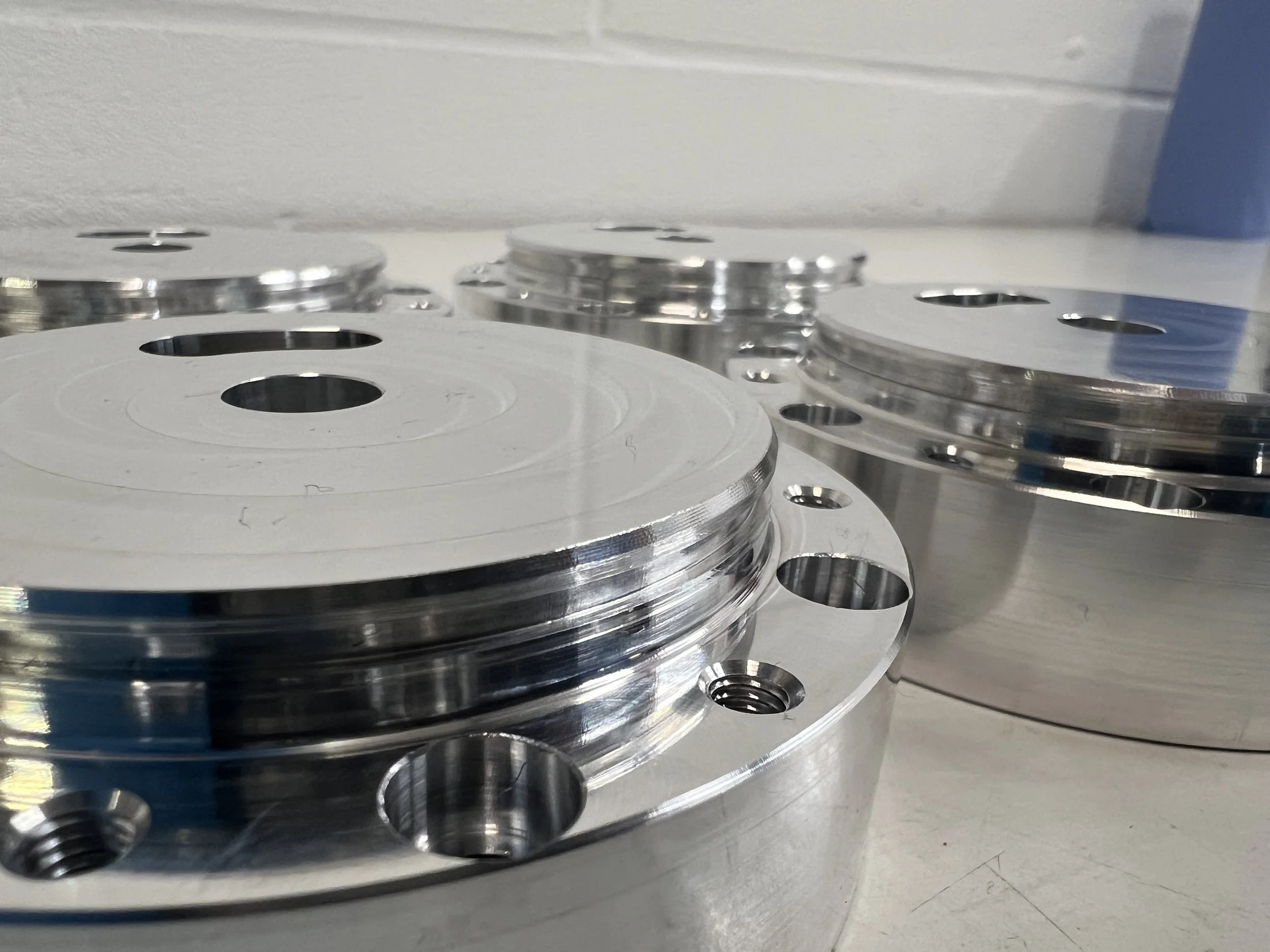 Stacks of shiny metal circular disks with holes around the edges, placed on a white surface against a plain wall.