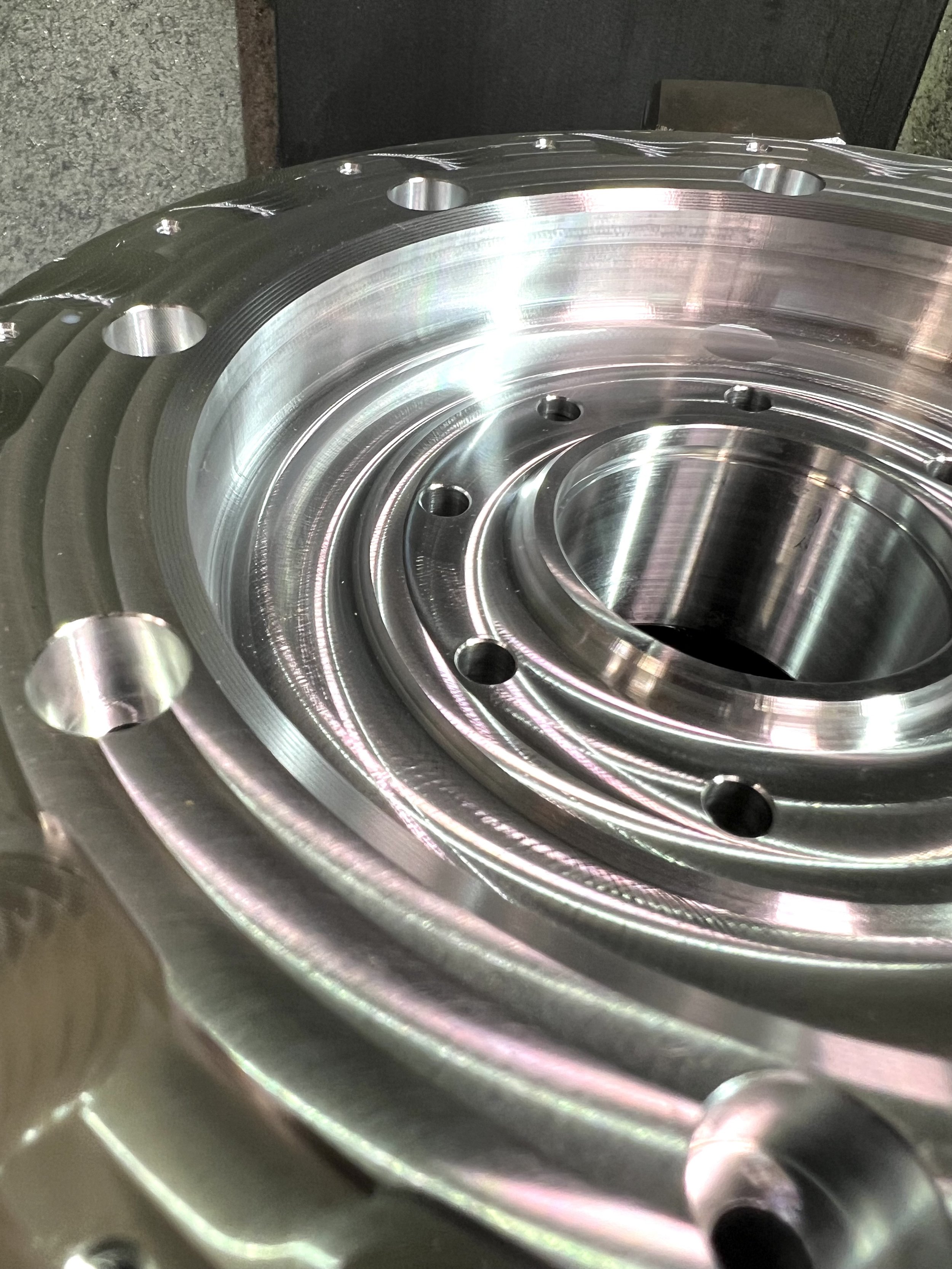 Close-up of a shiny, metallic mechanical part with circular grooves, holes, and a central shaft, likely a component of machinery or engine.