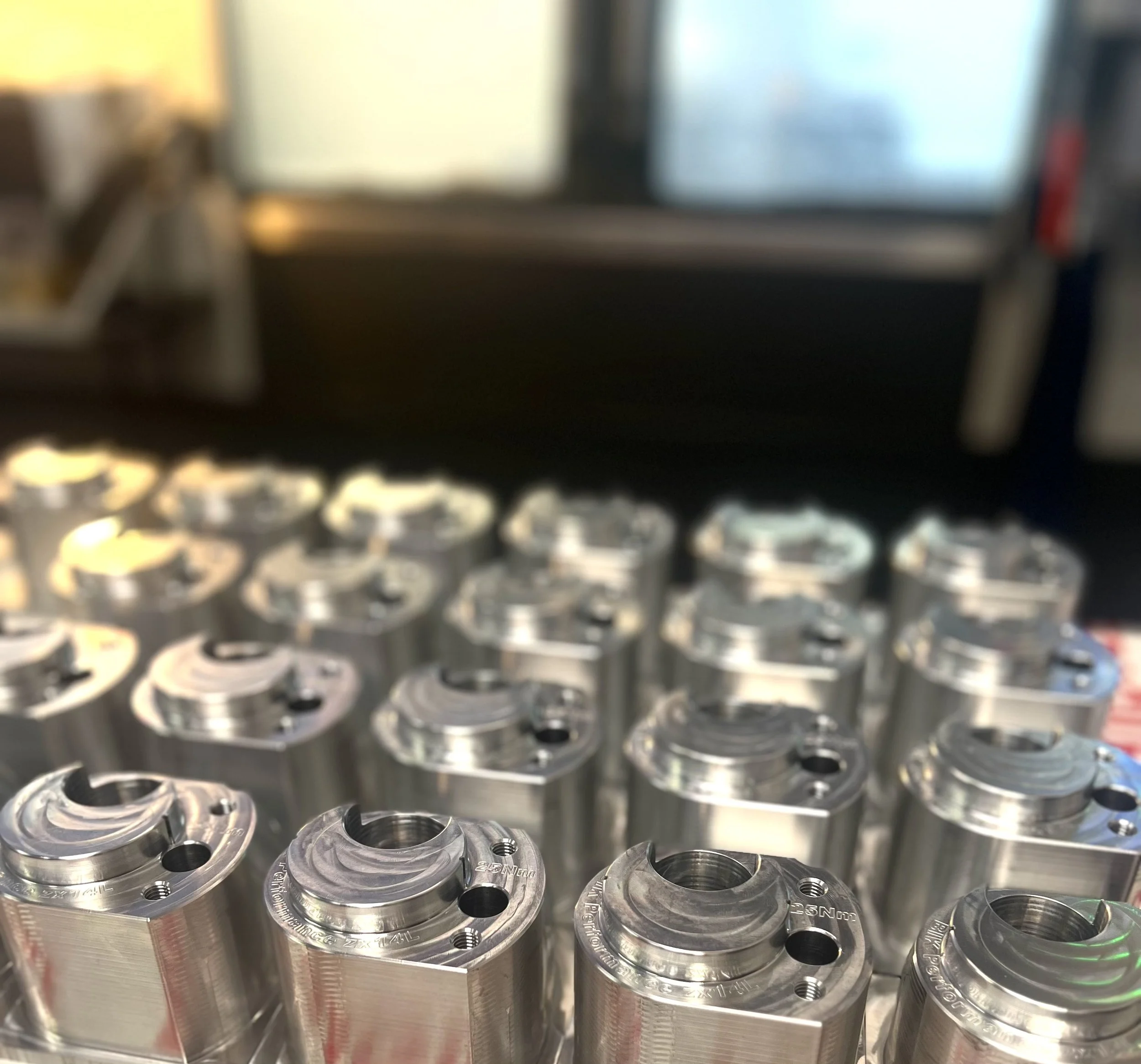 Multiple new, shiny metal mechanical parts arranged on a surface with a blurred industrial background.