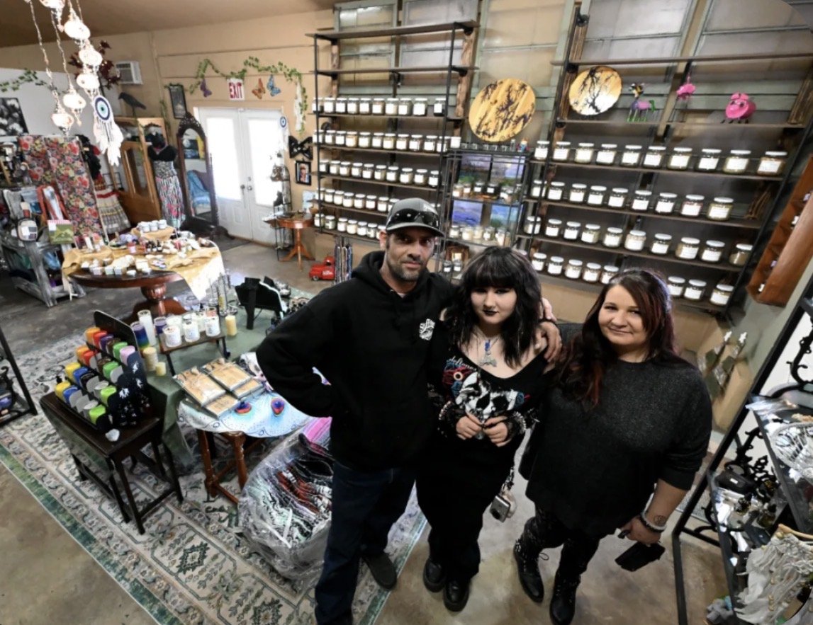 Three people standing inside a boutique store surrounded by jewelry, candles, and decorative items.