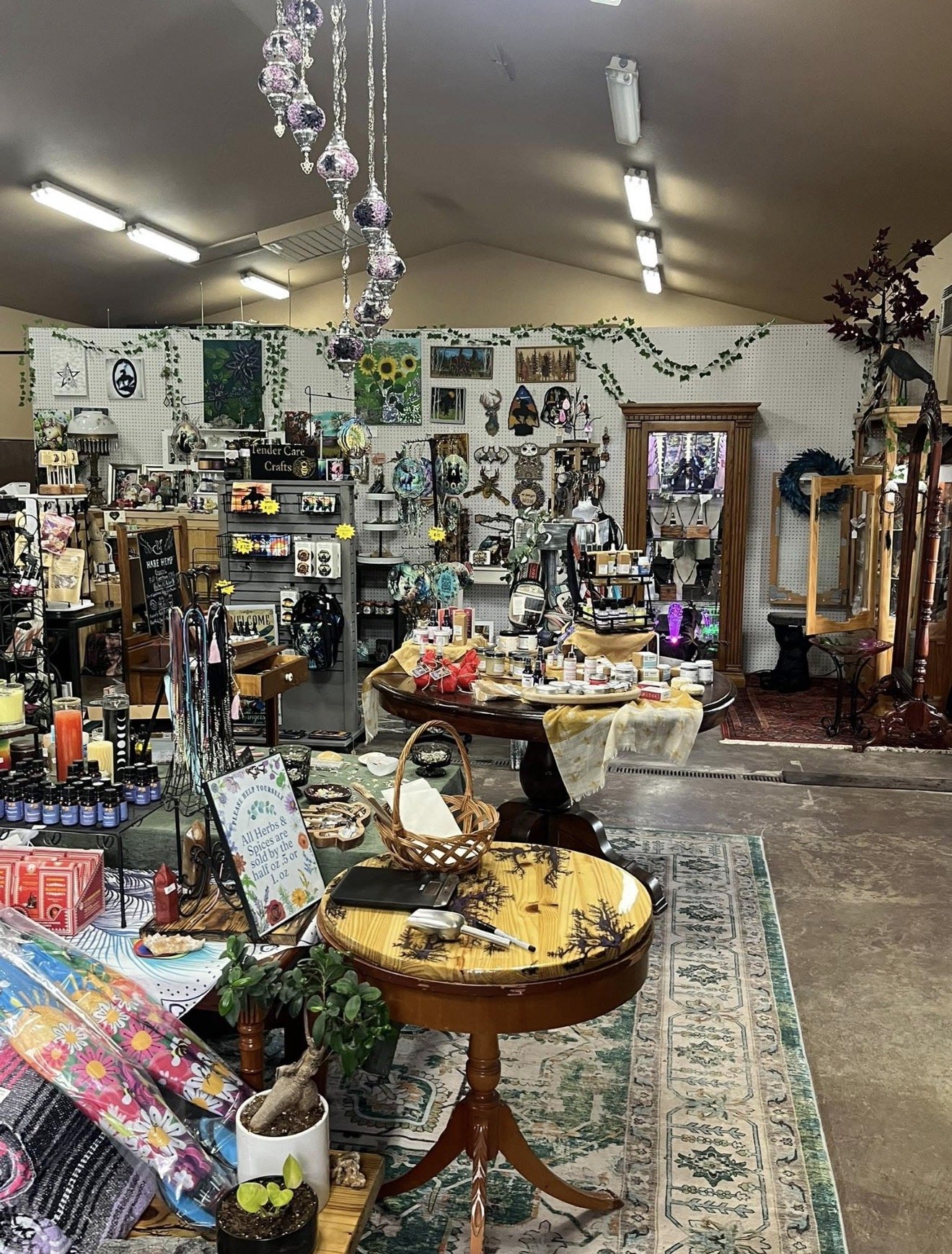 Interior of a gift or craft shop with various jewelry, candles, and decorative items on shelves and tables, hanging ornaments from the ceiling, and a mirror in the back.