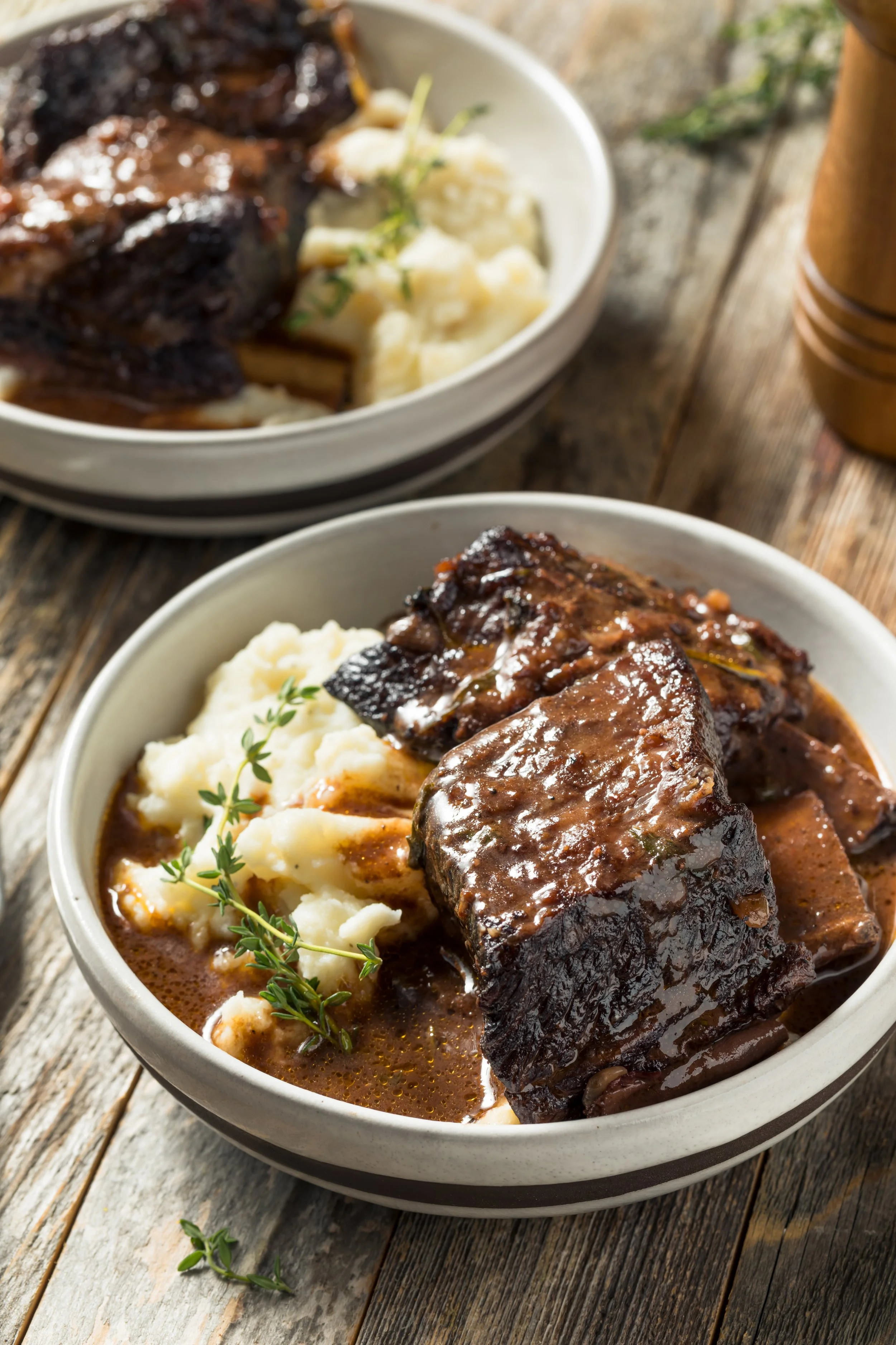 Bowl of beef stew with chunks of beef, mashed potatoes, and garnished with herbs, served on a rustic wooden table.