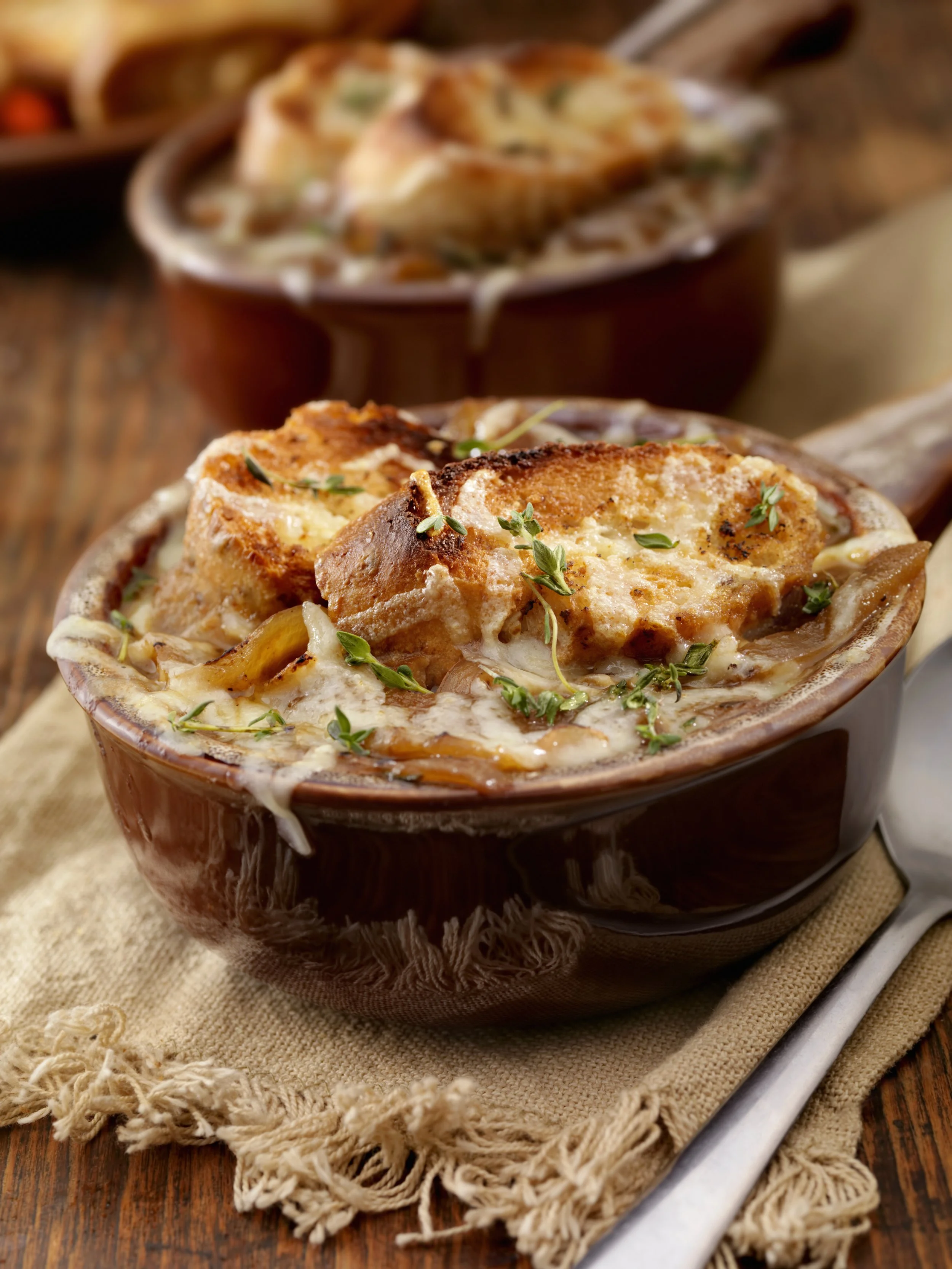 Baked French onion soup with melted cheese and fresh herbs in a brown bowl on a wooden table.