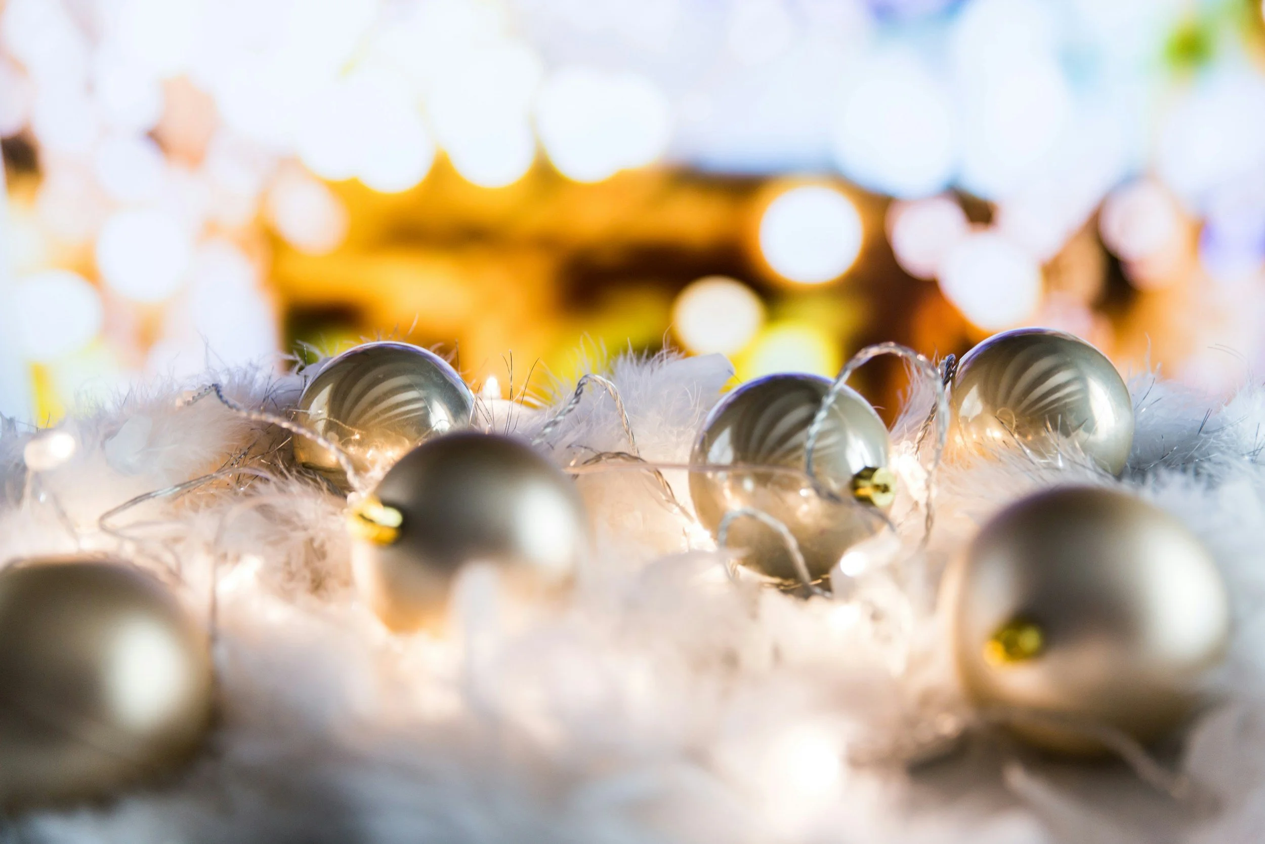 Silver Christmas ornaments with string lights on a snowy surface with blurred colorful holiday background.