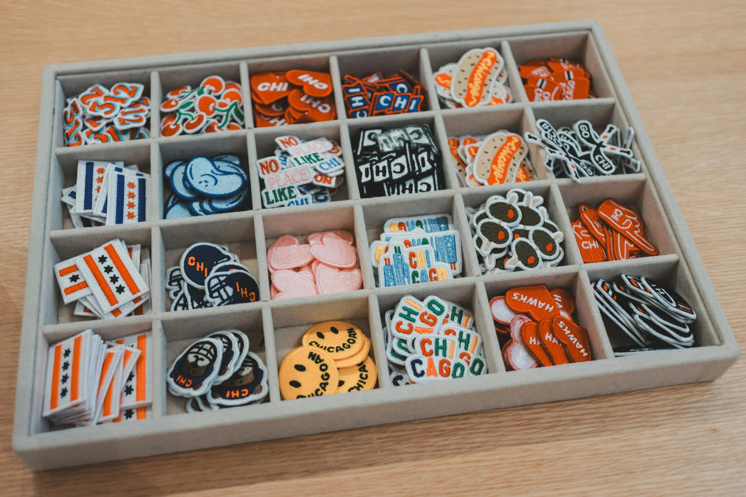 A storage box filled with small, colorful game tokens or patches, each with different designs and text, organized into individual compartments.