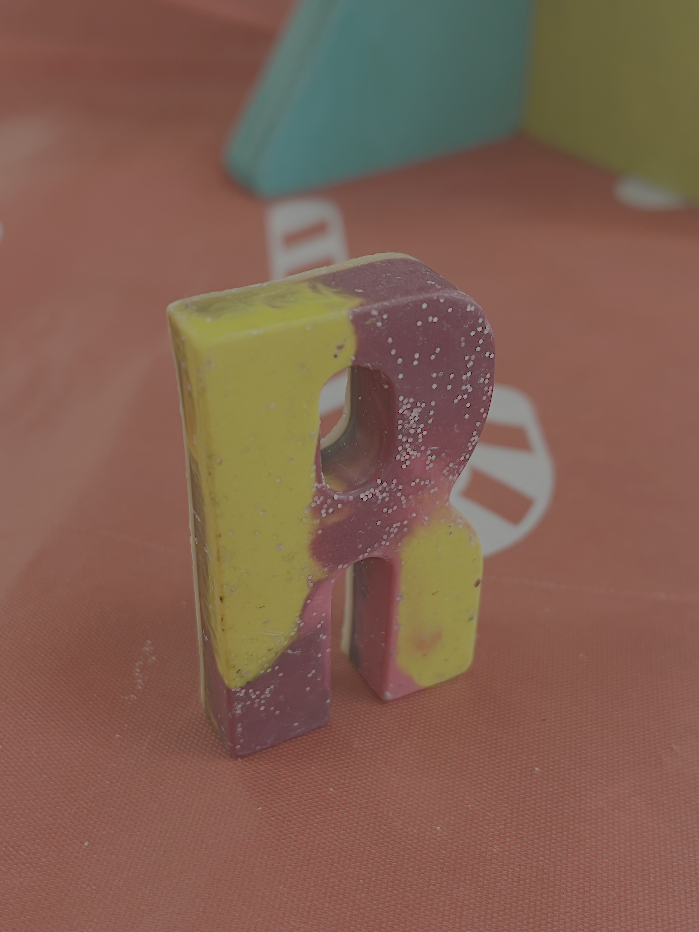 Painted plaster letter R on a pink surface, with blurred background.