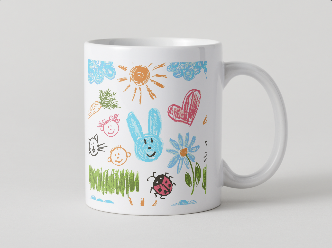 White ceramic mug with colorful, childlike drawings of a sun, clouds, a carrot, a pink heart, a blue bunny, a flower, a ladybug, a smiling face, a black cat, and green grass.