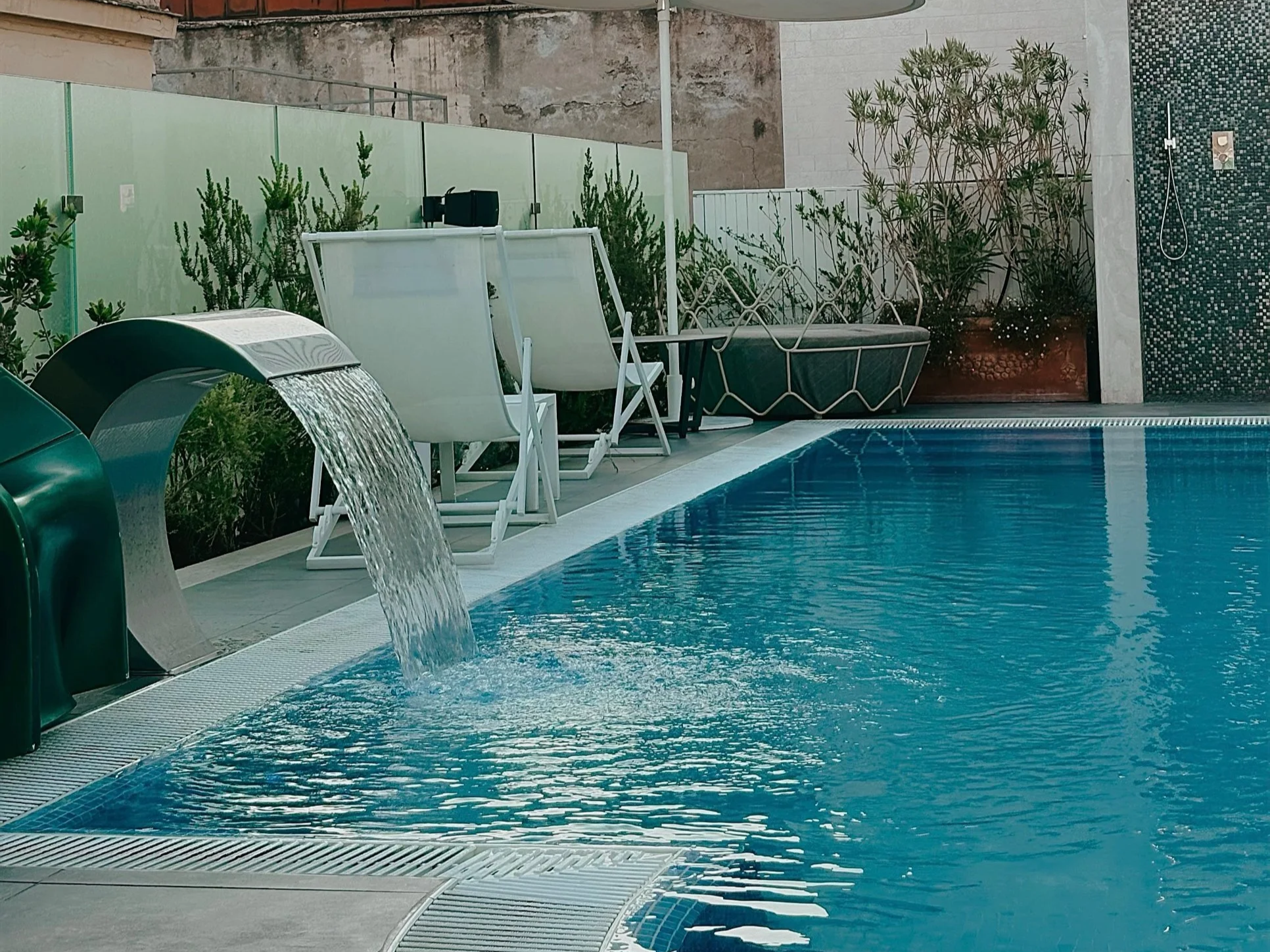 Small rooftop plunge pool with a waterfall feature and loungers at Aleph Rome Hotel near Via Veneto
